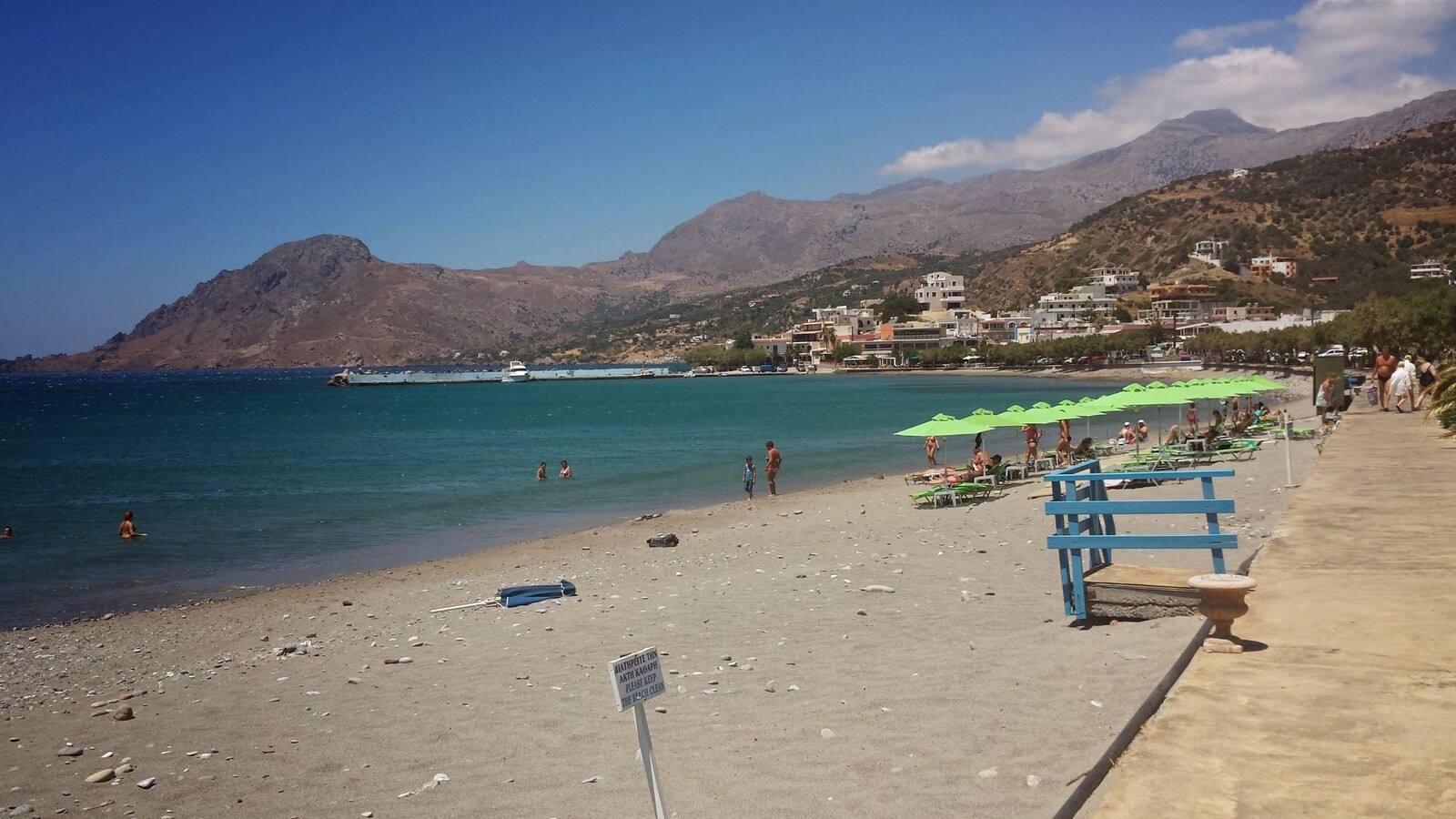 Una giornata pigra tra ombrelloni verdi e mare turchese, sotto le montagne.