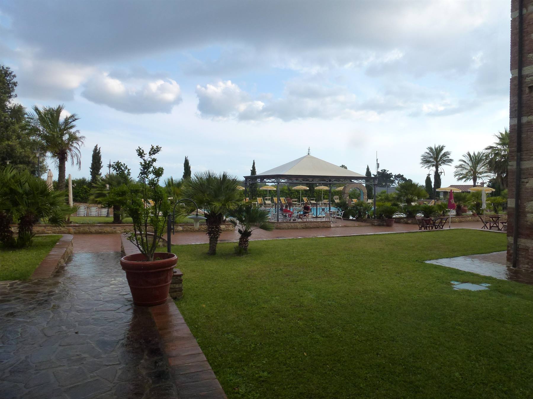Piscina con gazebo bianco tra palme e prato bagnato dopo la pioggia