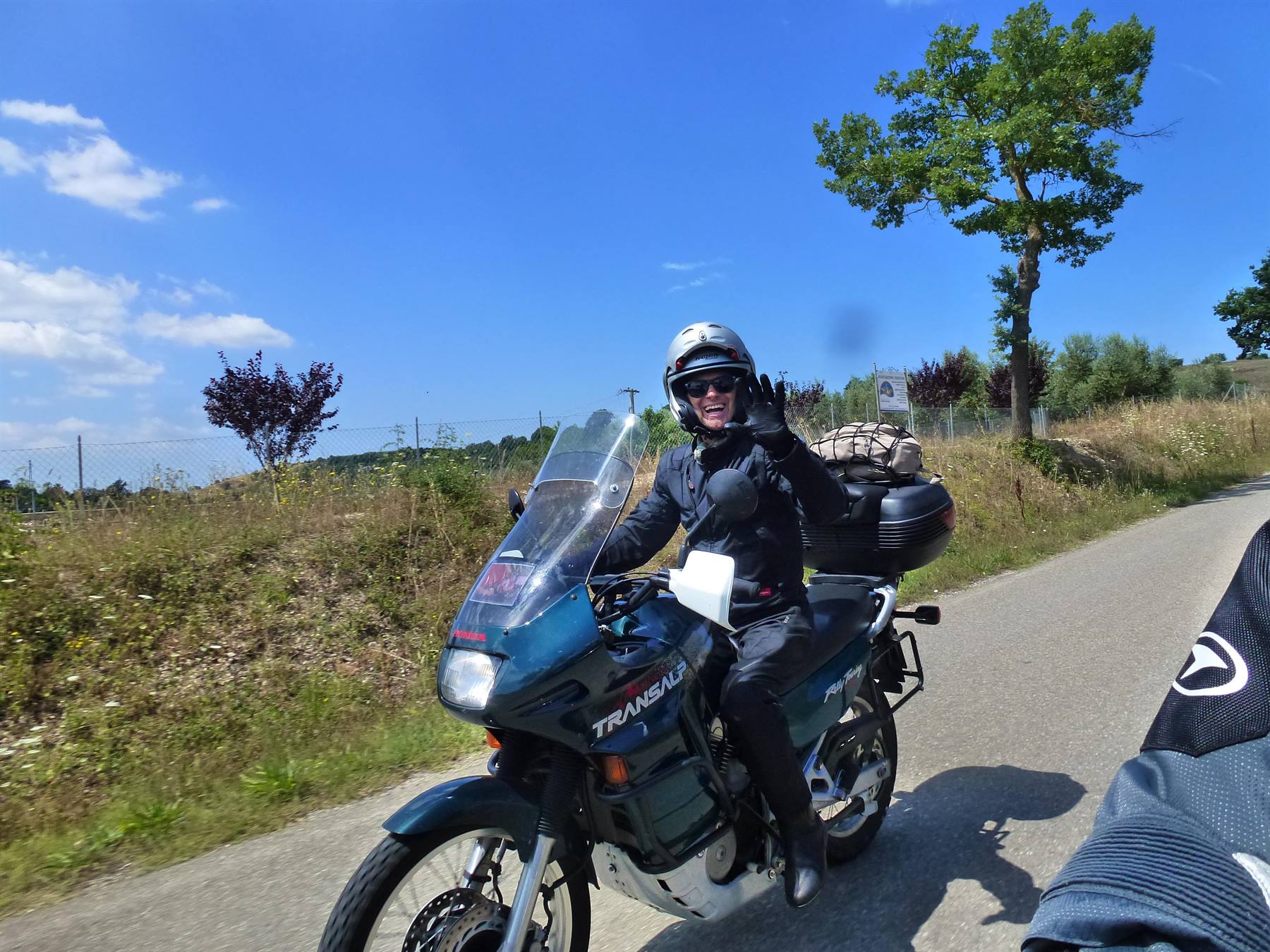 Motociclista con casco saluta in sella a una Honda Transalp verde su strada di campagna