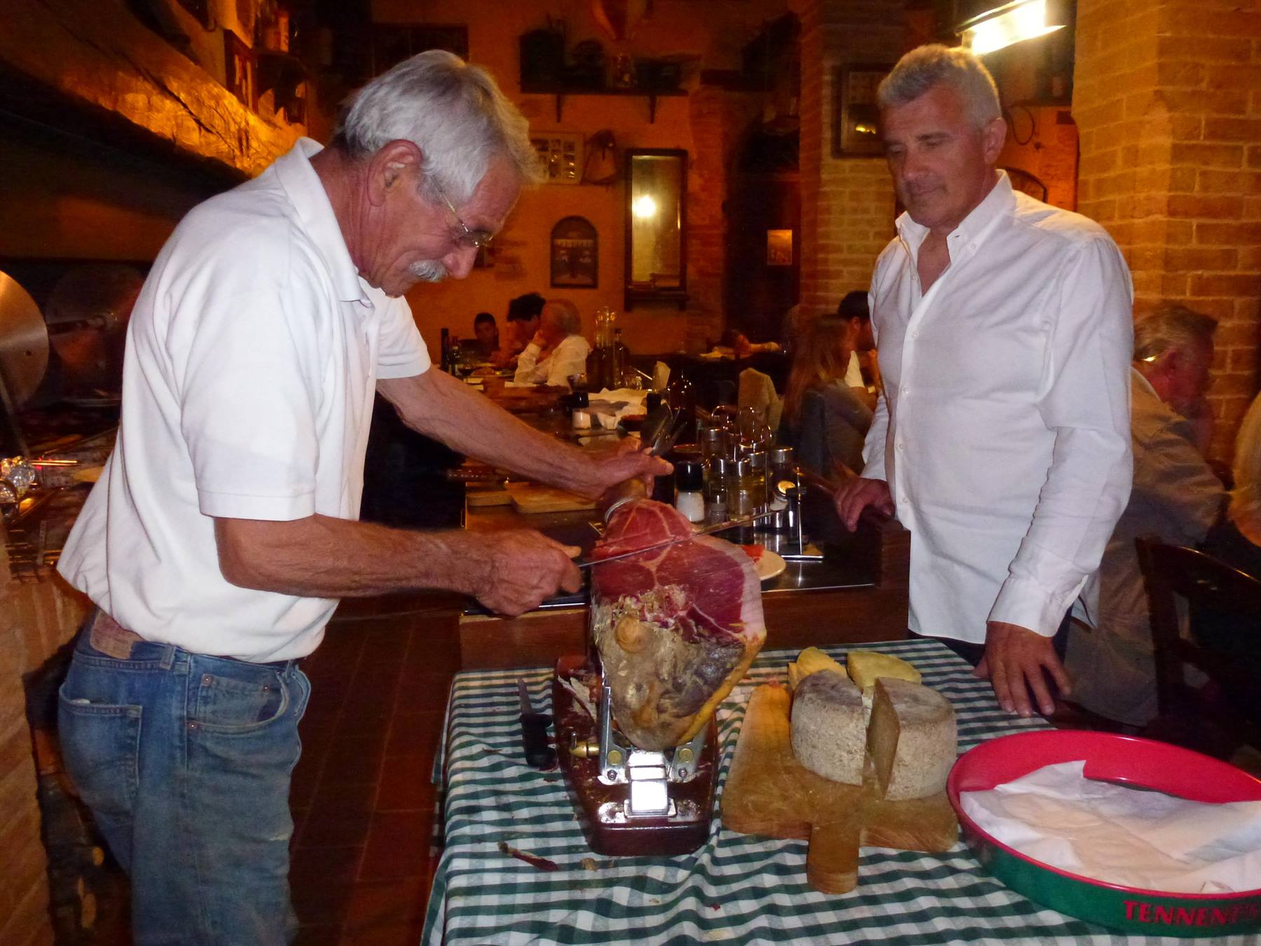 Due uomini in trattoria tagliano prosciutto con formaggio sul tavolo