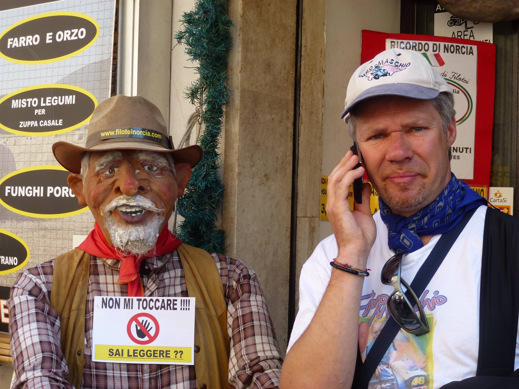 Turista al telefono accanto a un finto pastore di Norcia con cartello non toccare