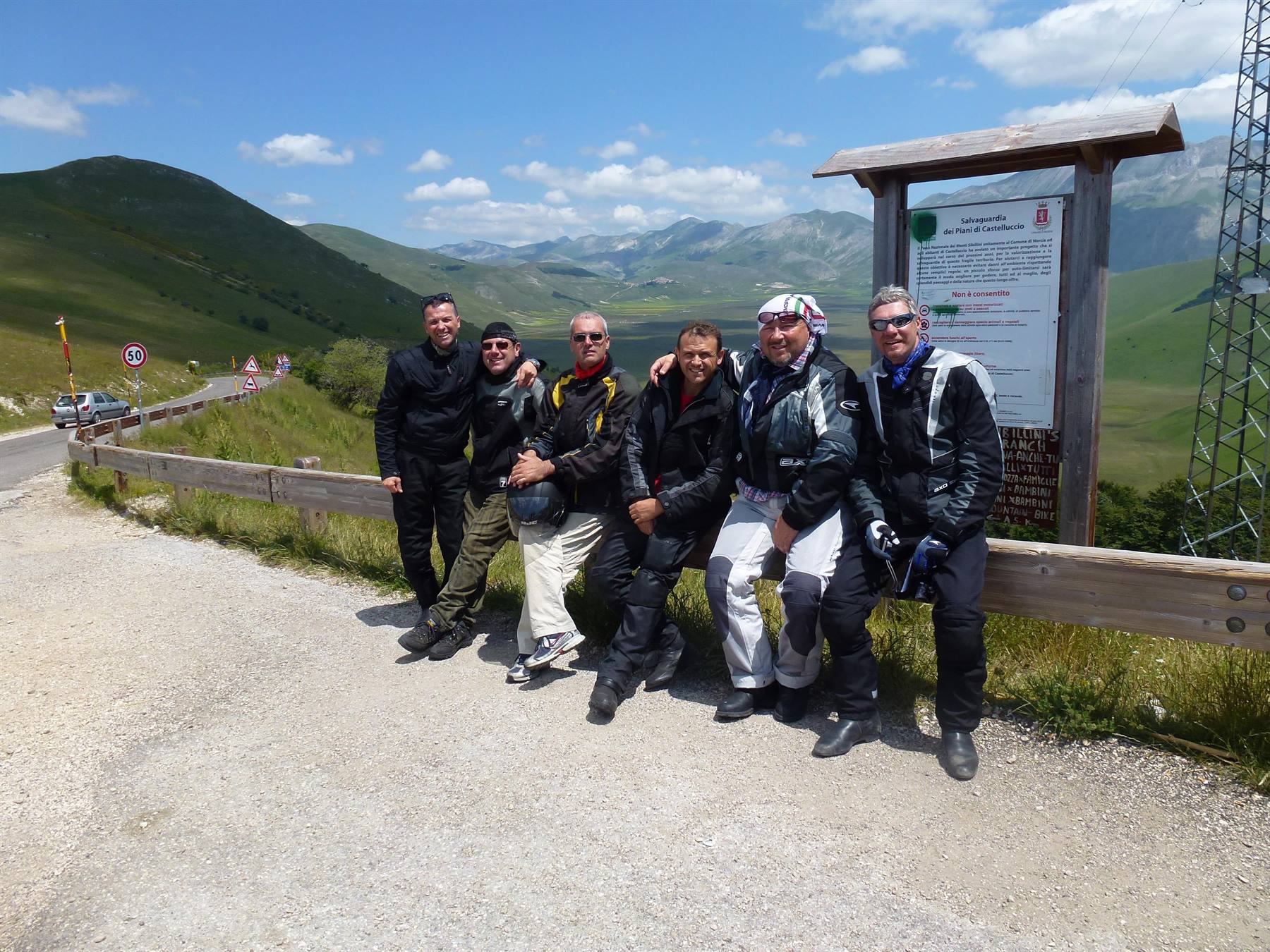Sei motociclisti posano accanto a un cartello in legno sui monti Sibillini