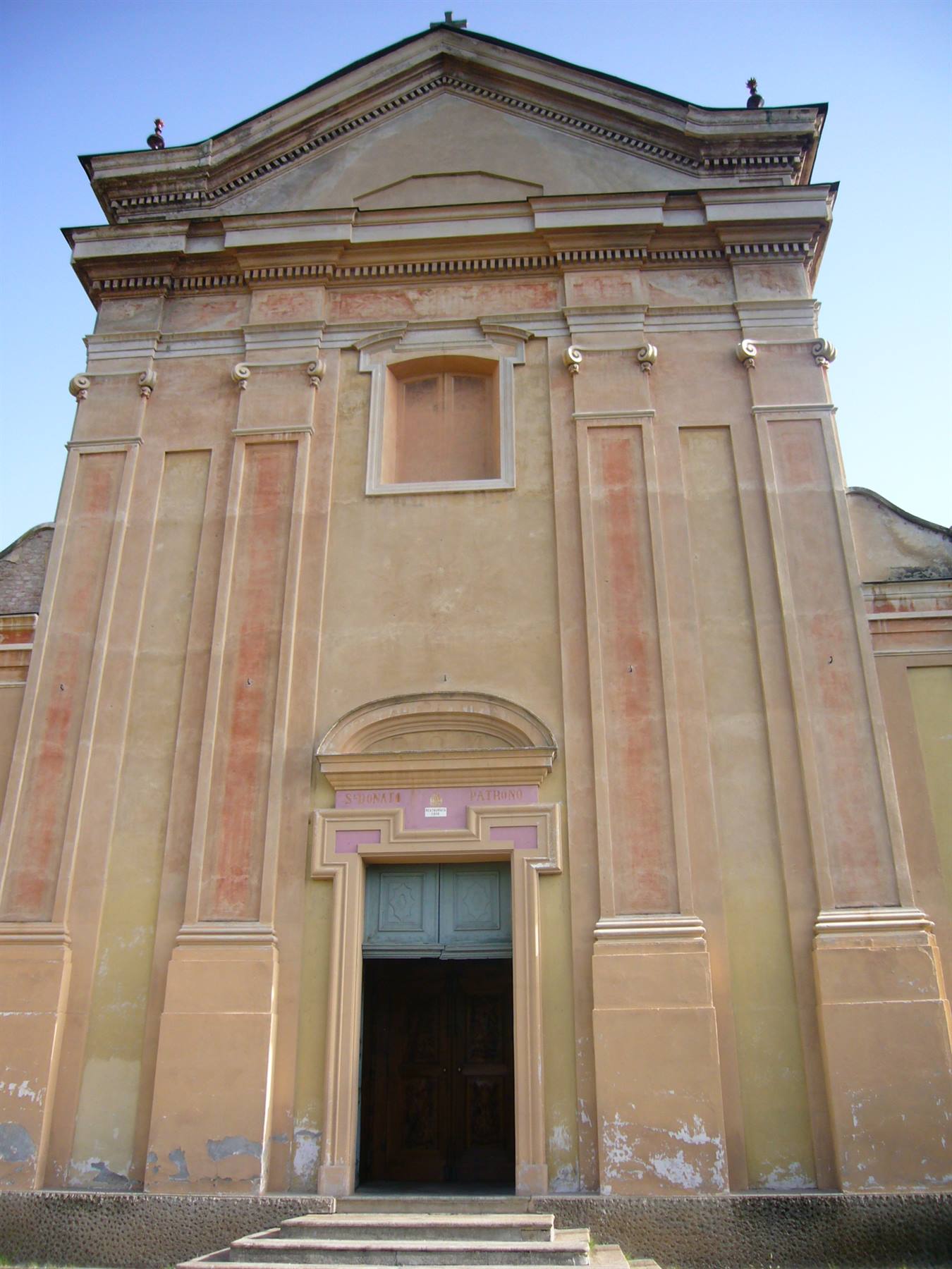 Facciata ocra di una chiesa con portone verde socchiuso e scalini in pietra