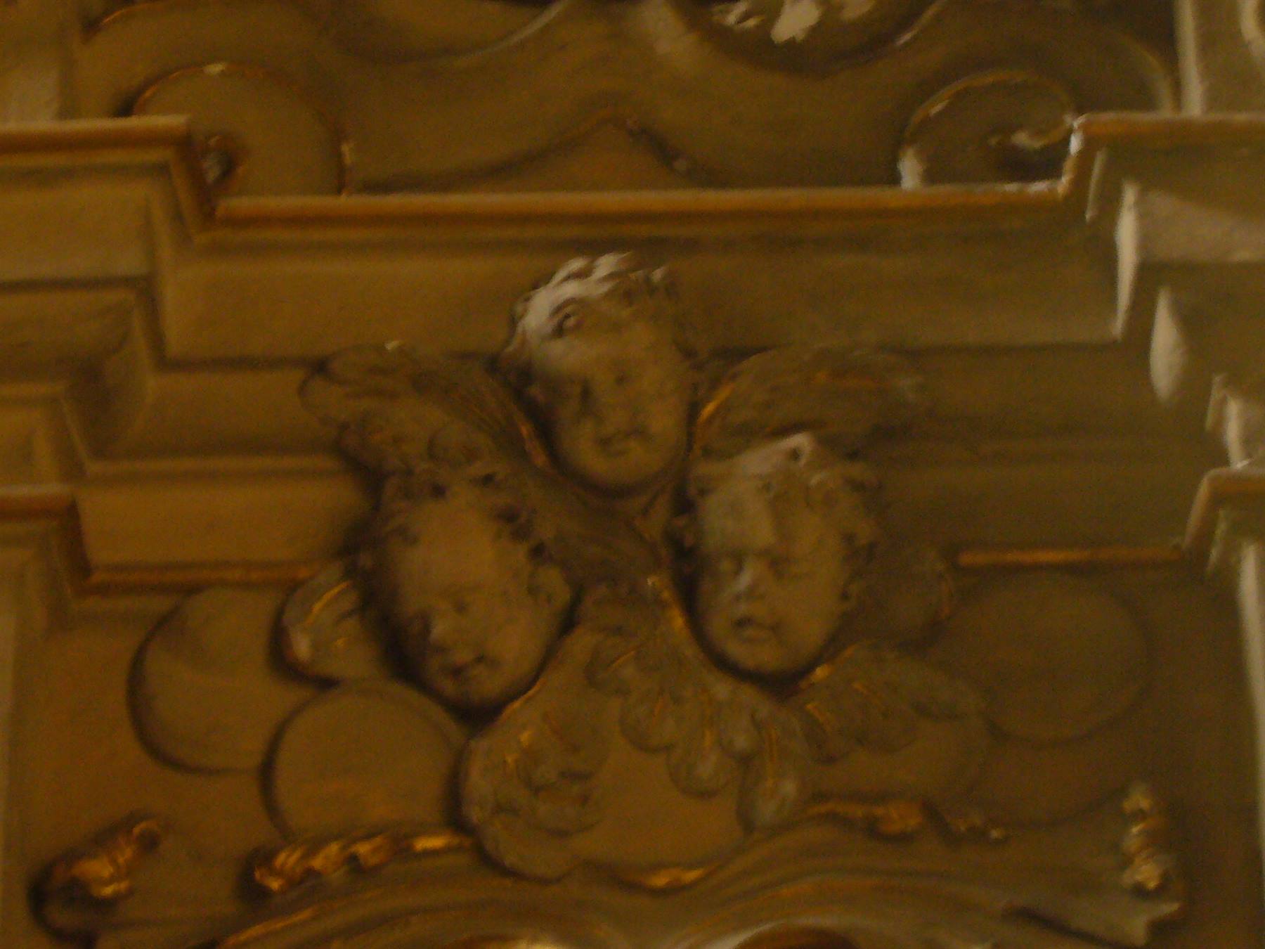 Tre putti scolpiti in legno dorato barocco, luce calda da chiesa