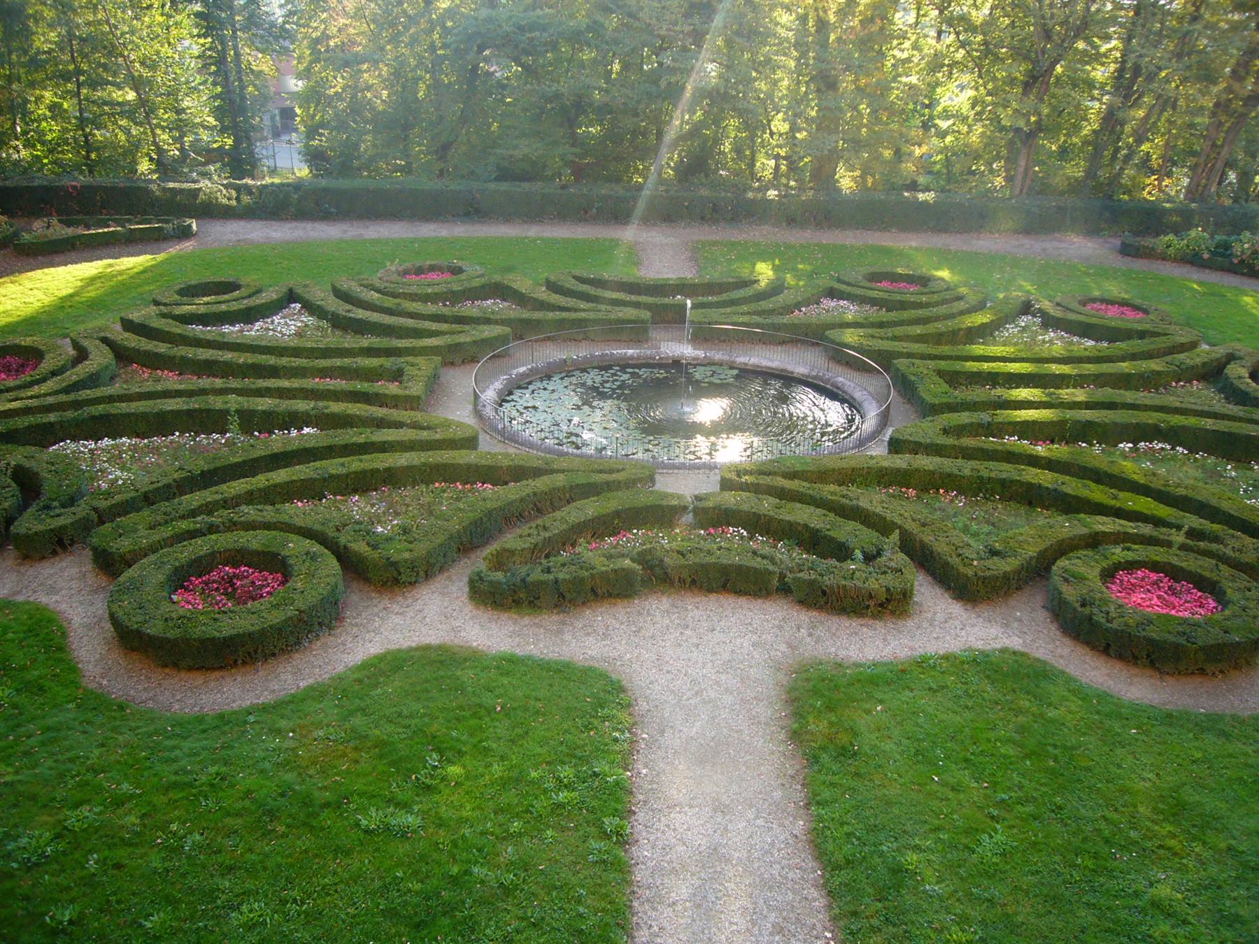 Fontana centrale in giardino formale, siepi geometriche a cordoli verde con fiori rossi