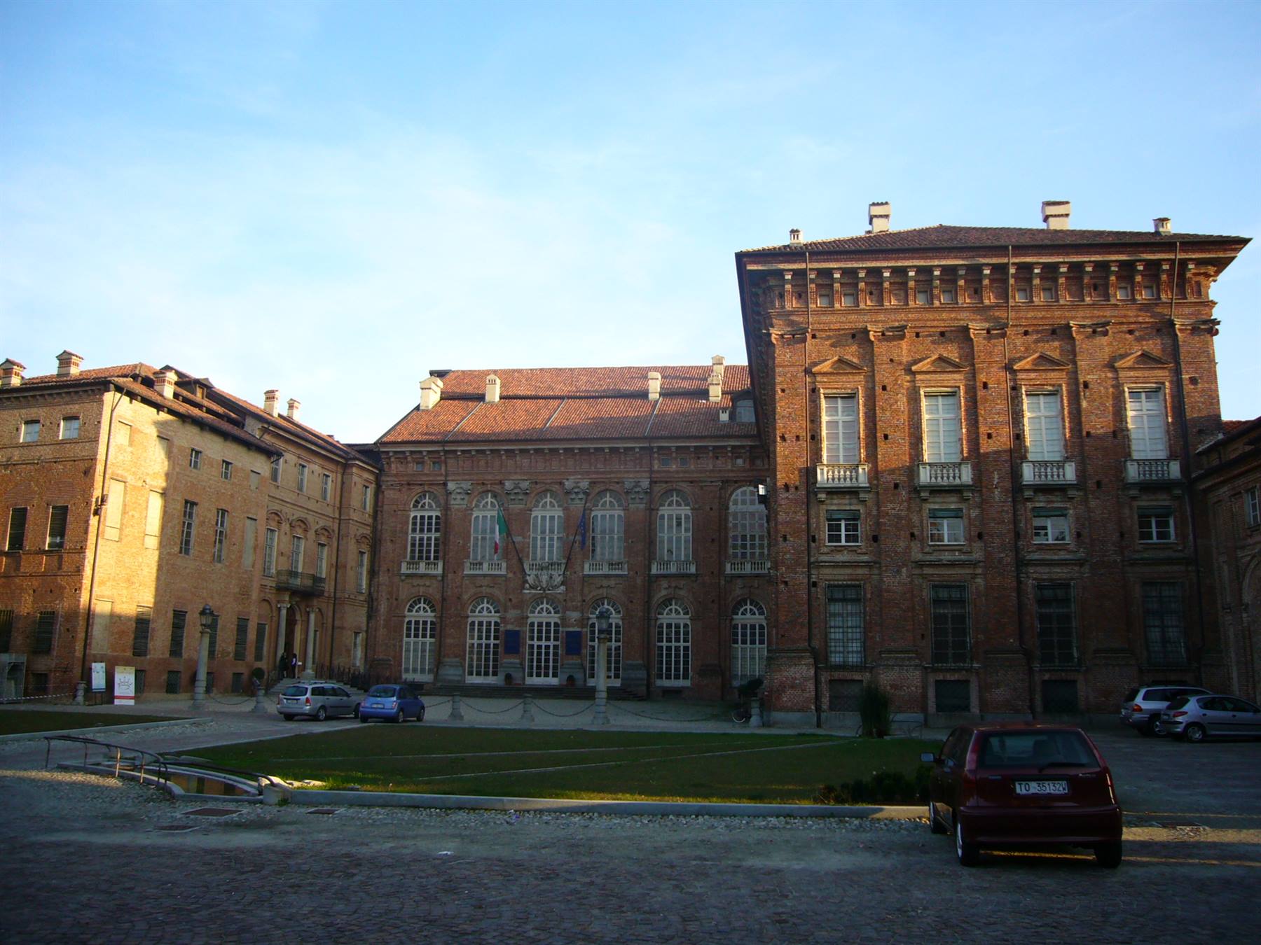 Castello di Racconigi, facciata in mattoni al sole, auto parcheggiate sulla piazza