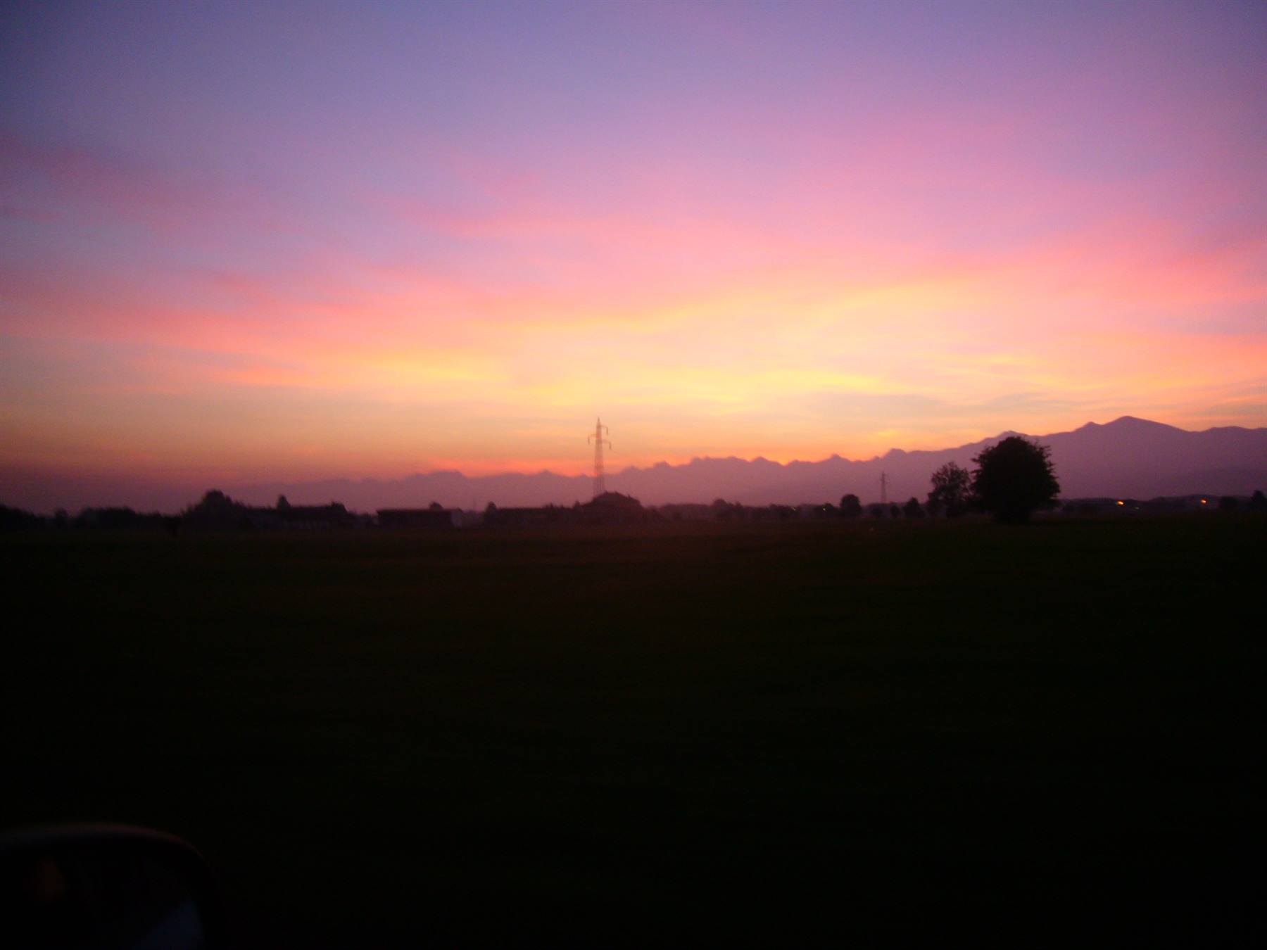Cielo rosa e viola sopra campi scuri e monti in lontananza