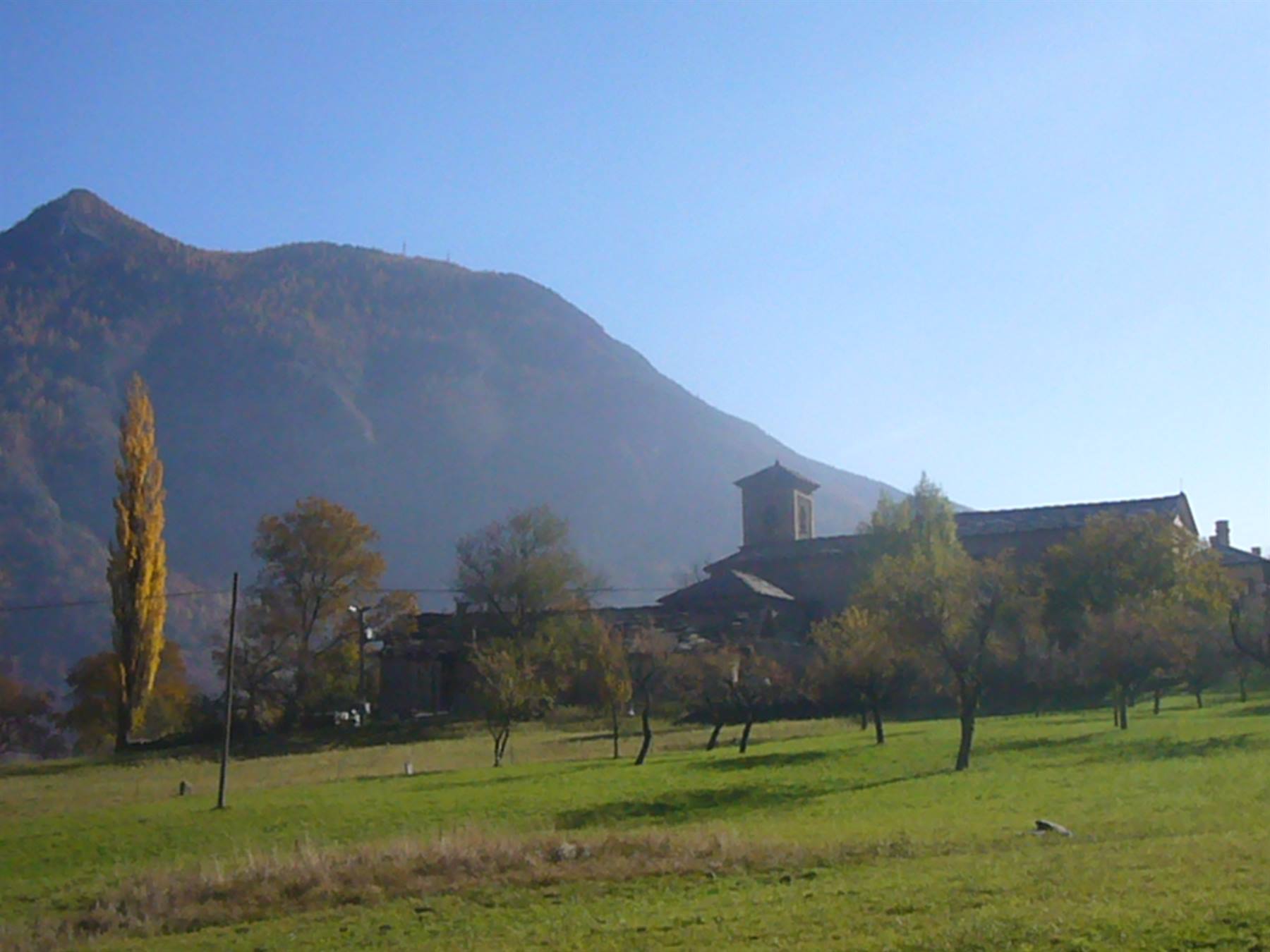 campanile di pietra tra gli alberi d'autunno, prato verde sotto la montagna