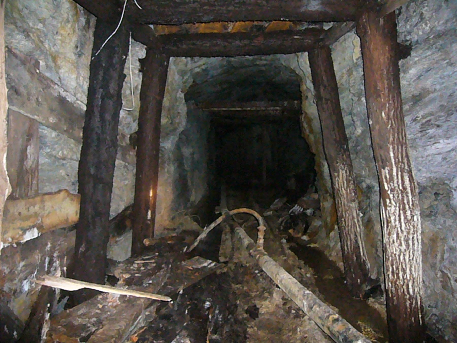 Galleria mineraria abbandonata con travi in legno e rotaie arrugginite