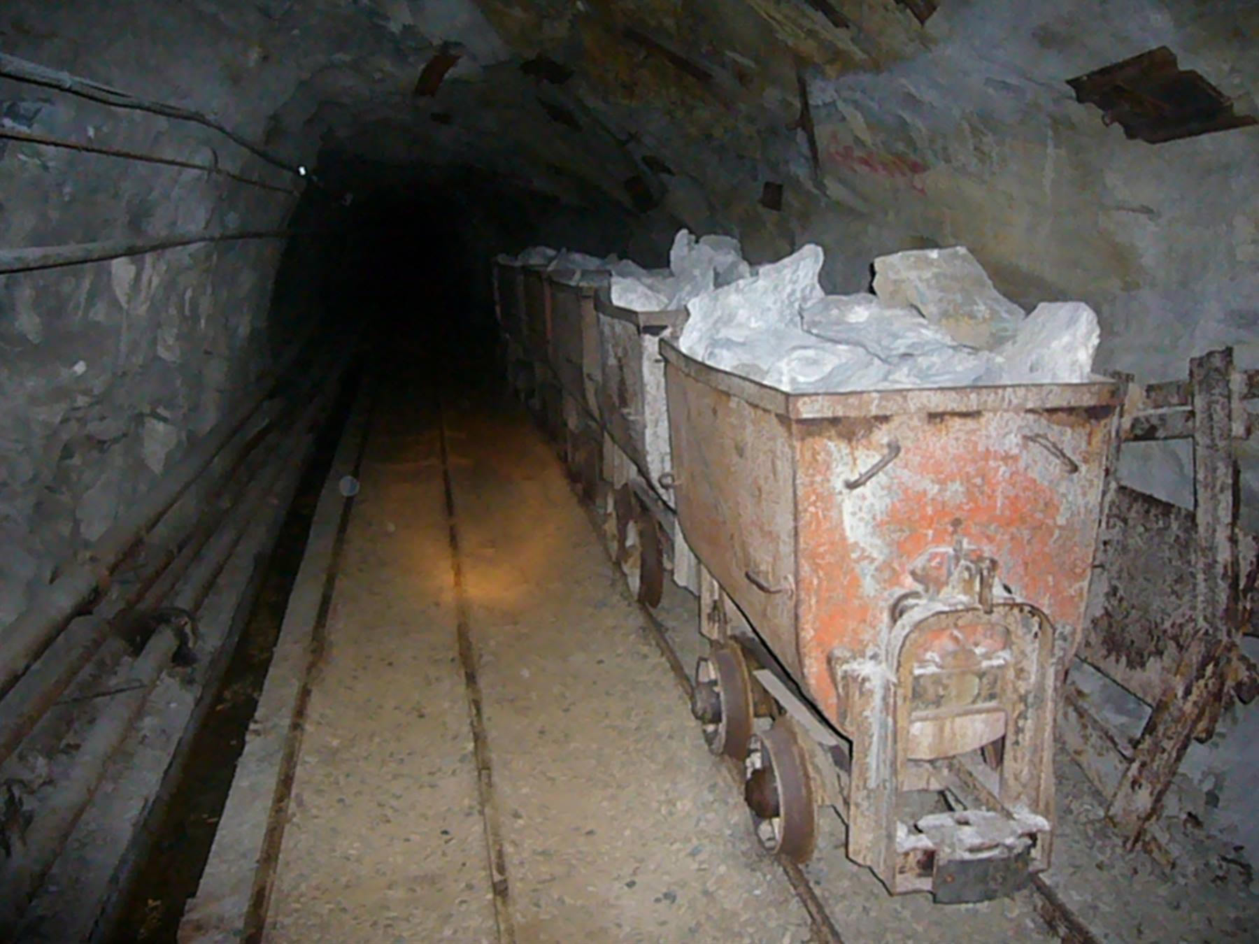 Vagoni arrugginiti carichi di minerale bianco dentro una galleria mineraria buia