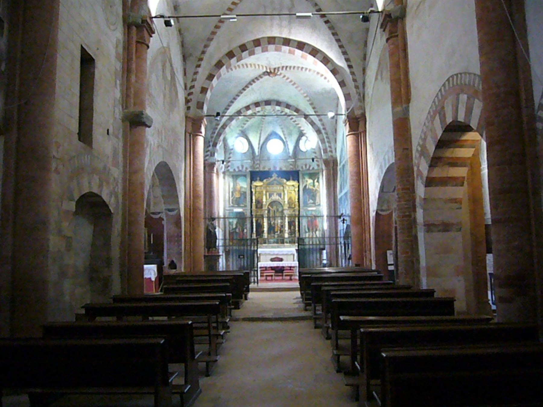 Interno di chiesa romanica con navate, colonne in cotto, altare e dipinto