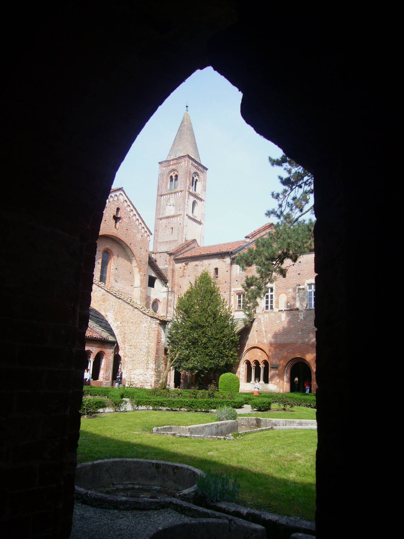 Chiostro in mattoni con campanile romanico visto attraverso un arco buio
