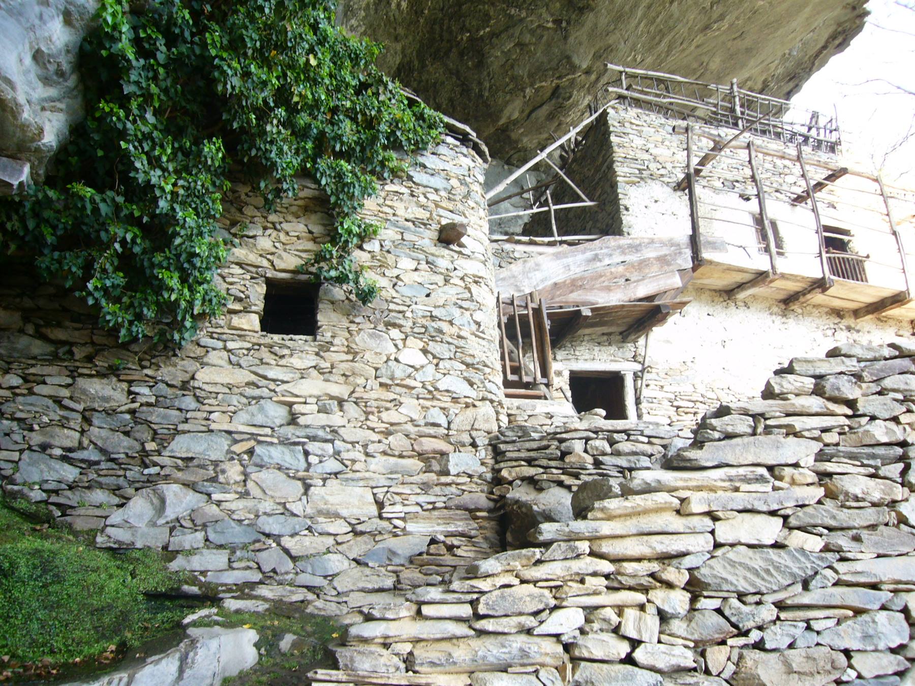 Case in pietra a secco sotto una sporgenza rocciosa, scale in pietra, edera verde