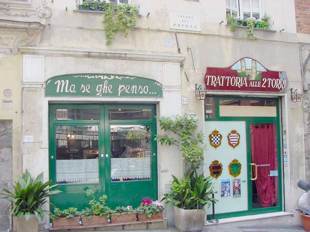 Facciata della Trattoria alle 2 Torri, insegne verdi e rosse, vaso di fiori