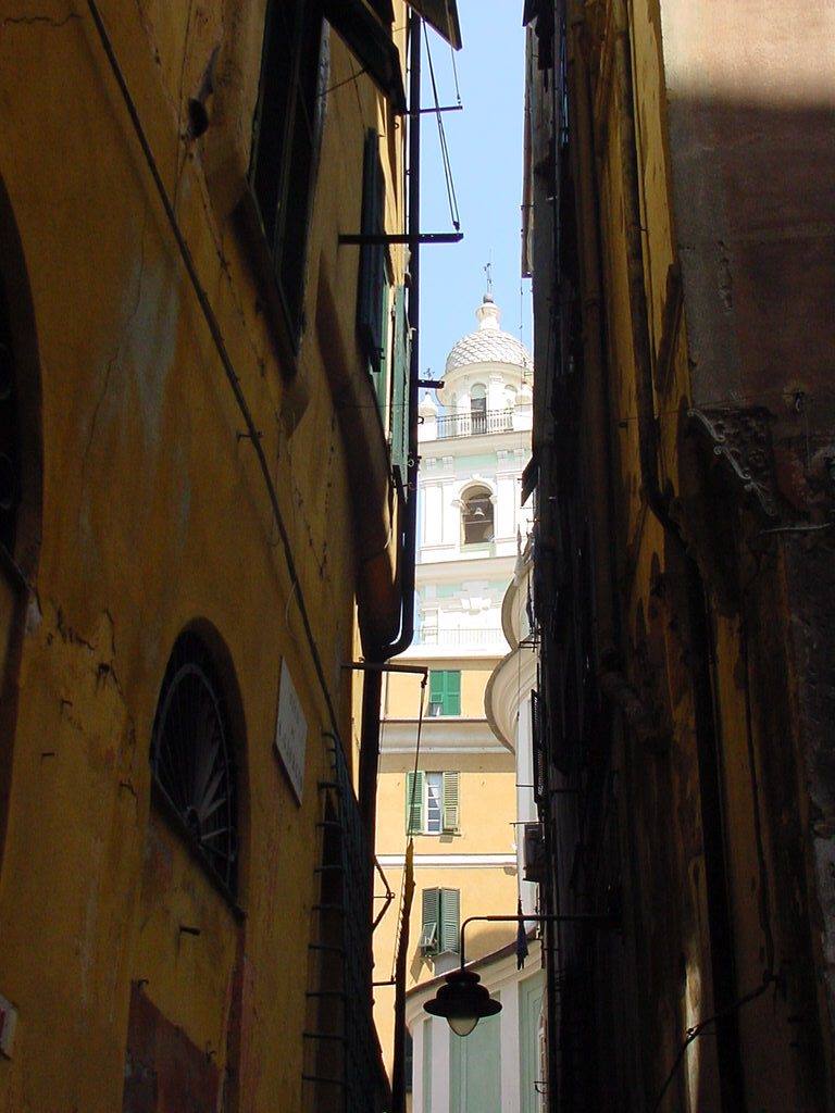 Vicolo stretto tra case ocra, campanile e cupola della chiesa, Genova