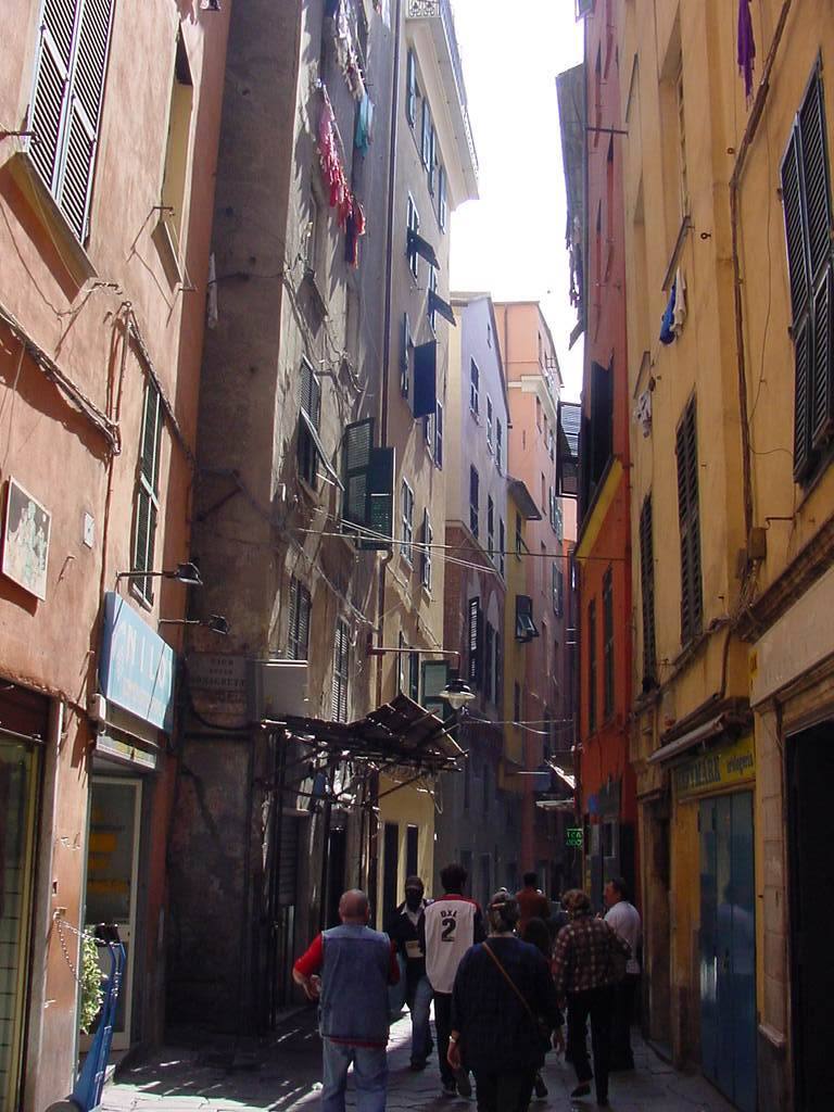 Pedoni in un vicolo stretto tra case colorate con persiani e panni appesi