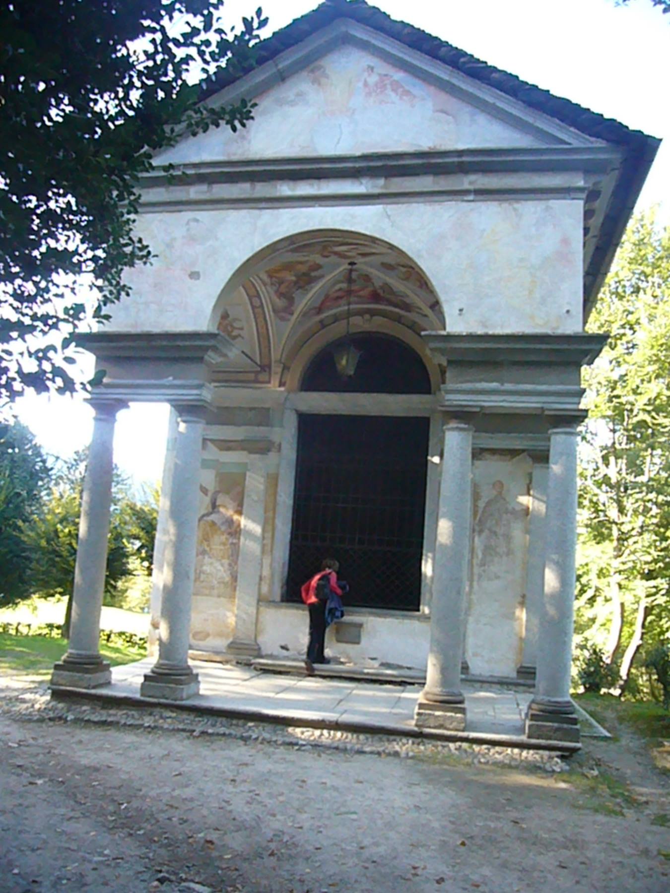 Turista con zaino osserva una cappella affrescata con colonne in pietra