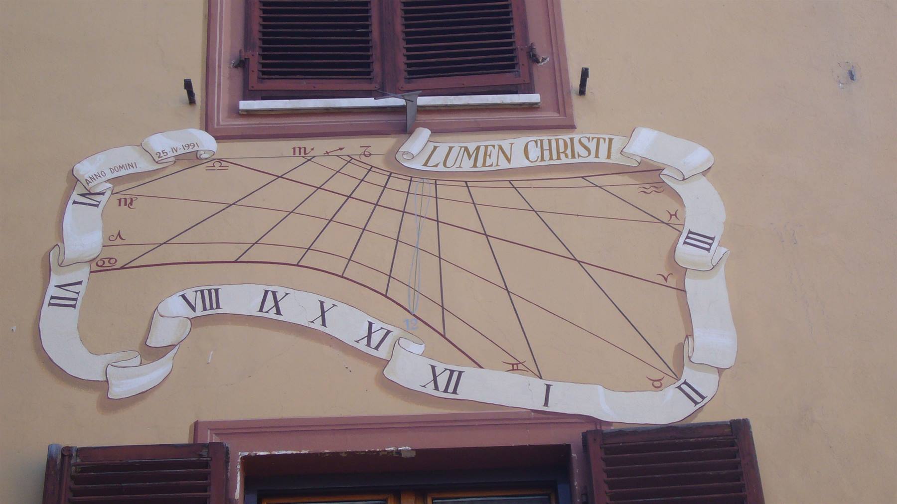 Meridiana dipinta con scritta Lumen Christi tra due finestre con persiane
