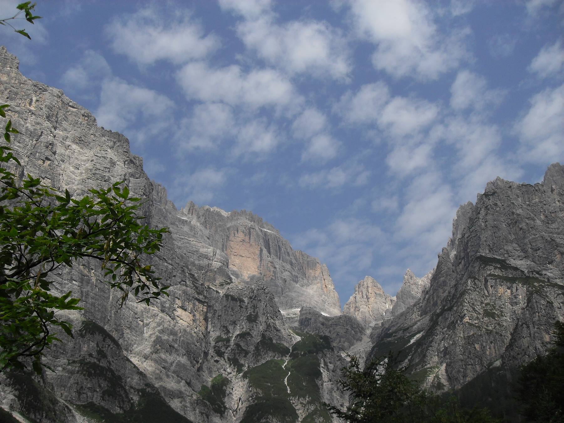 Pareti rocciose verticali sopra la valle, cielo azzurro con nuvole bianche