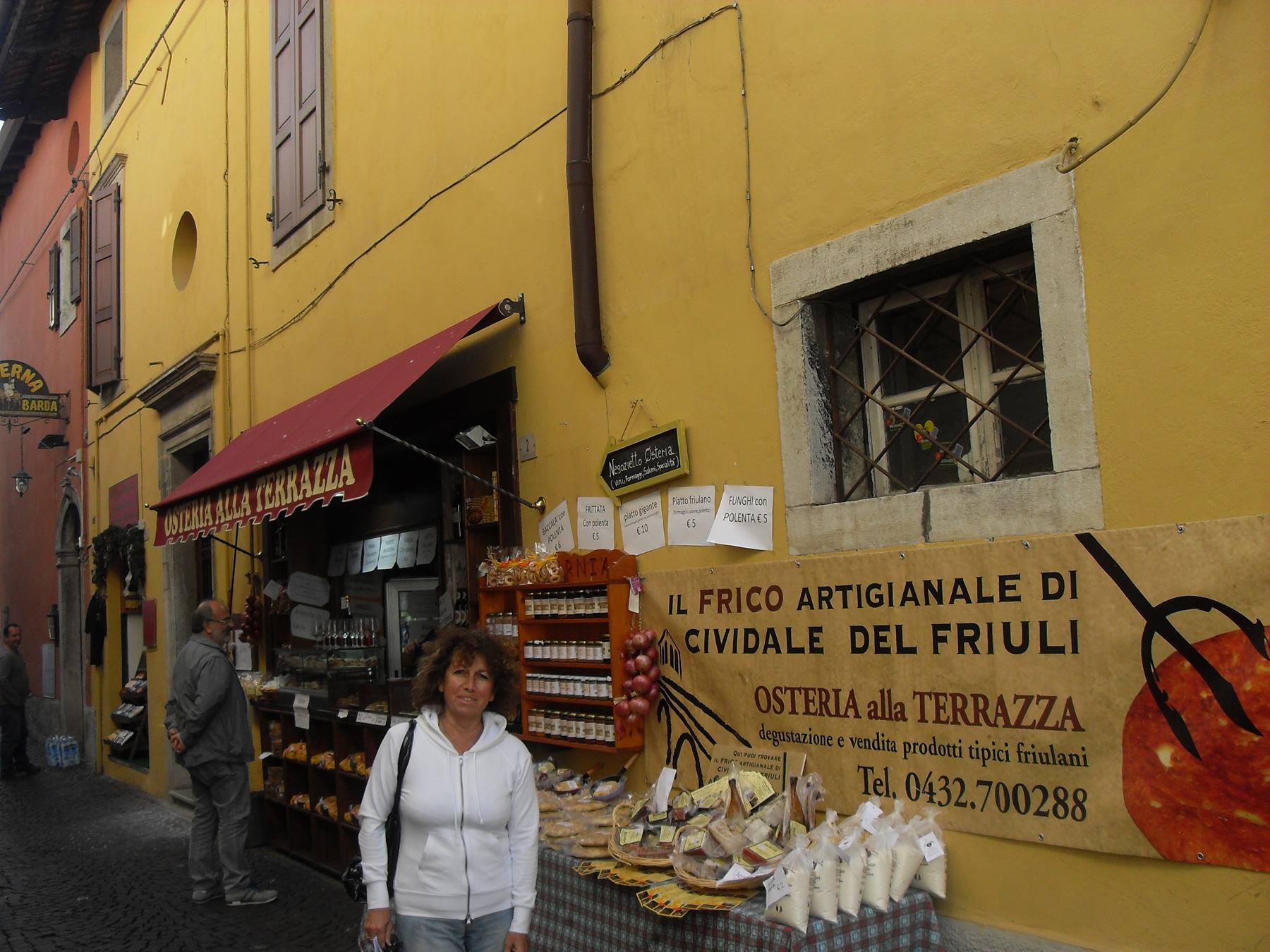 Donna davanti all'osteria alla Terrazza, bancarella di formaggi e salumi a Cividale del Friuli
