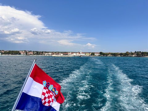Addio alla costa istriana: la scia del traghetto e la bandiera croata al vento.