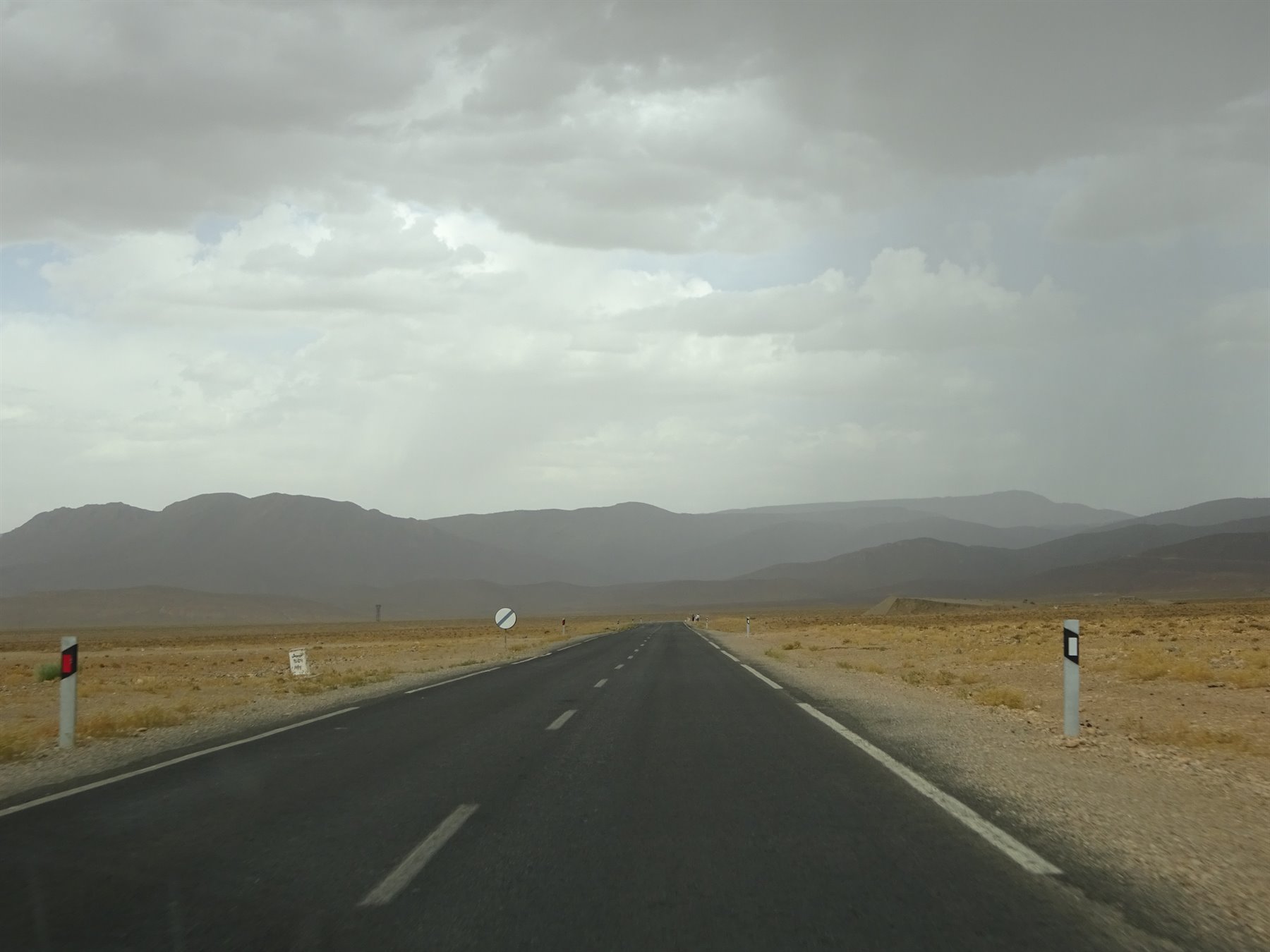 Strada asfaltata verso Errachidia tra steppe aride e montagne sotto nuvole grigie