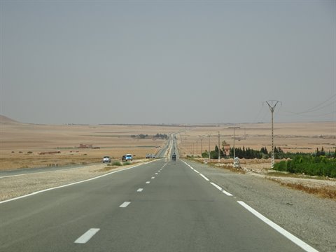 Strada dritta nel sud marocchino verso Errachidia, auto e tralicci tra campi aridi