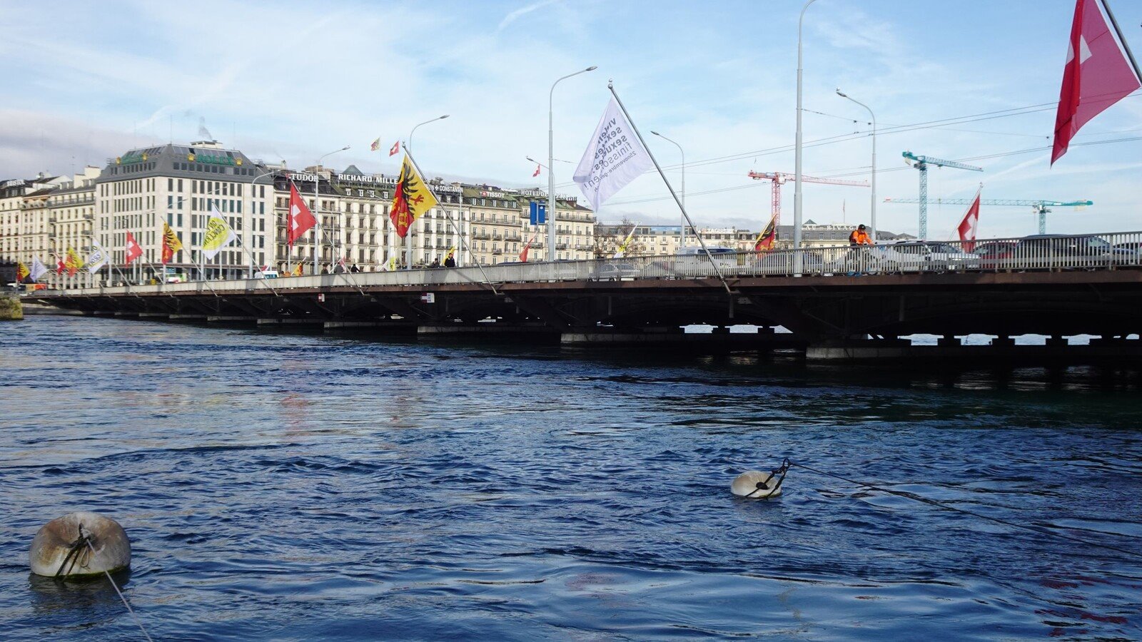 Il Rodano e il ponte di Ginevra, bandiere al vento in una mattina luminosa.