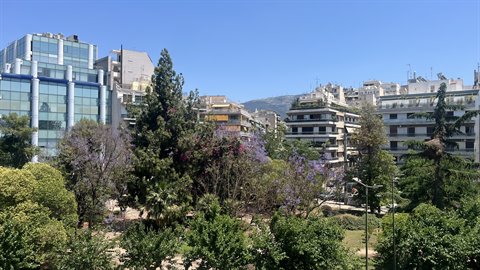 Atene dal balcone: cielo azzurro, montagne e alberi in fiore.