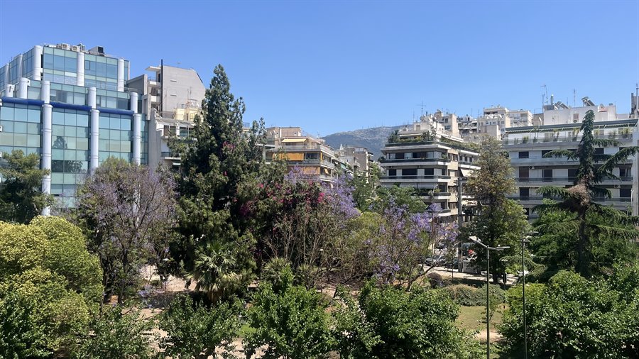 Atene dal balcone: cielo azzurro, montagne e alberi in fiore.