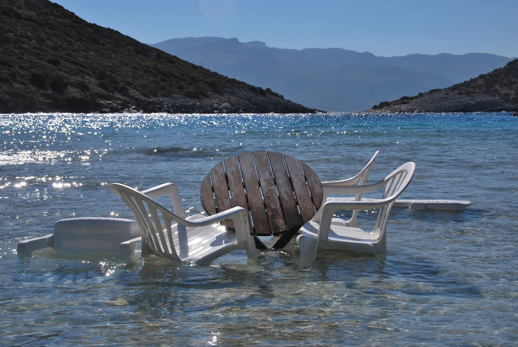 Tavolo di legno e sedie di plastica bianche immersi nell'acqua cristallina tra colline