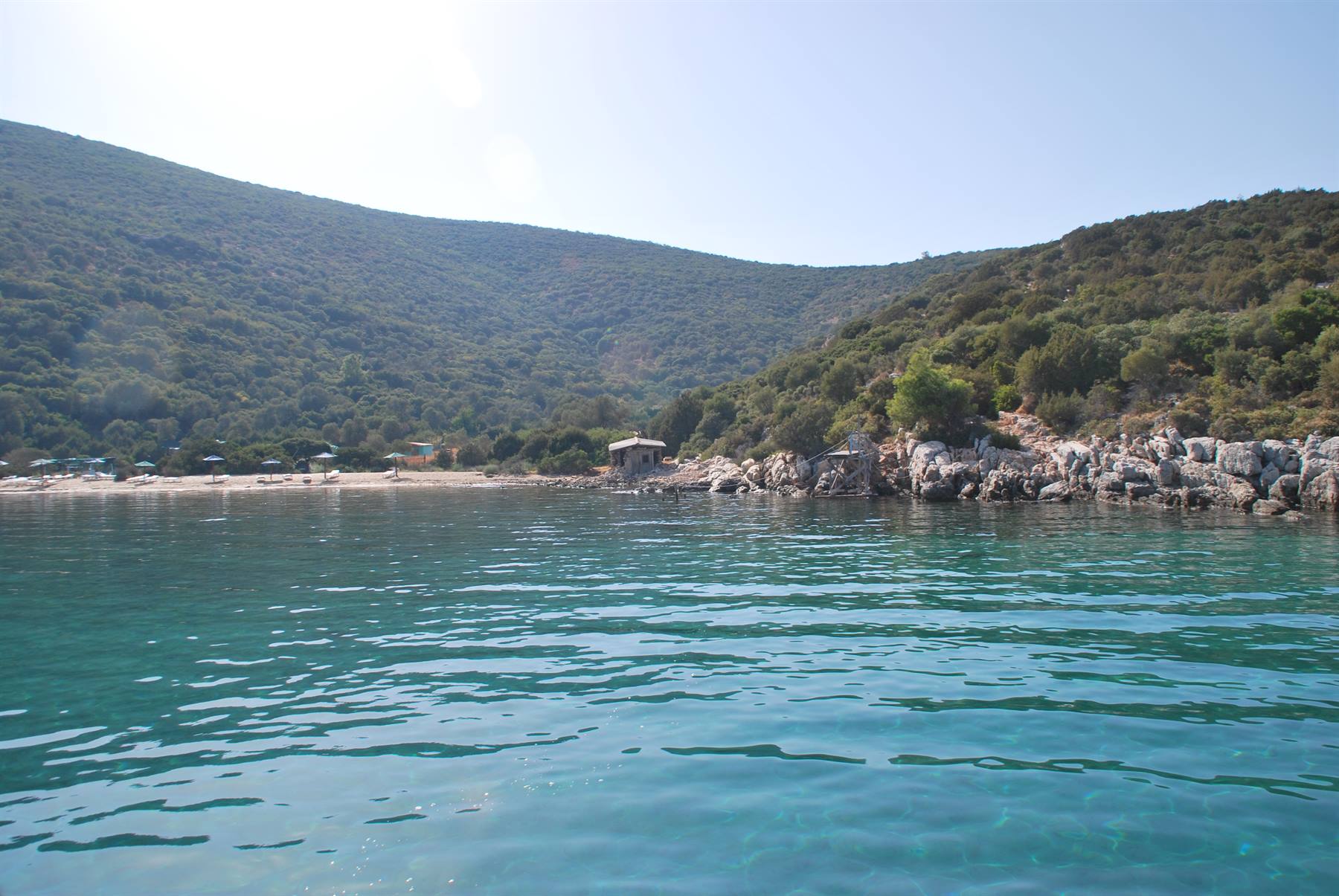Acqua turchese davanti a spiaggia sabbiosa e colline verdi con ombrelloni