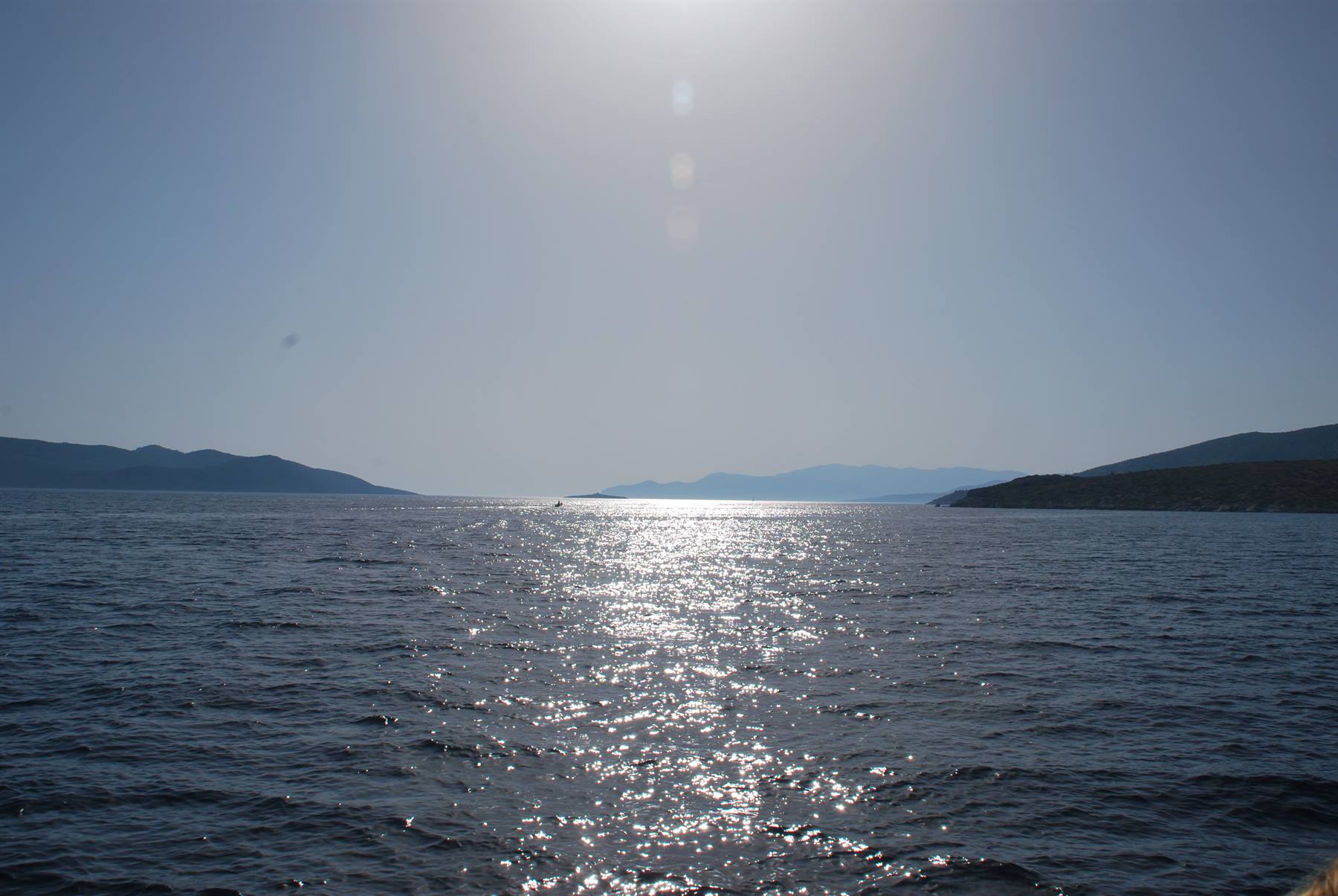 Sole alto sul mare, riflessi scintillanti sull'acqua tra colline scure