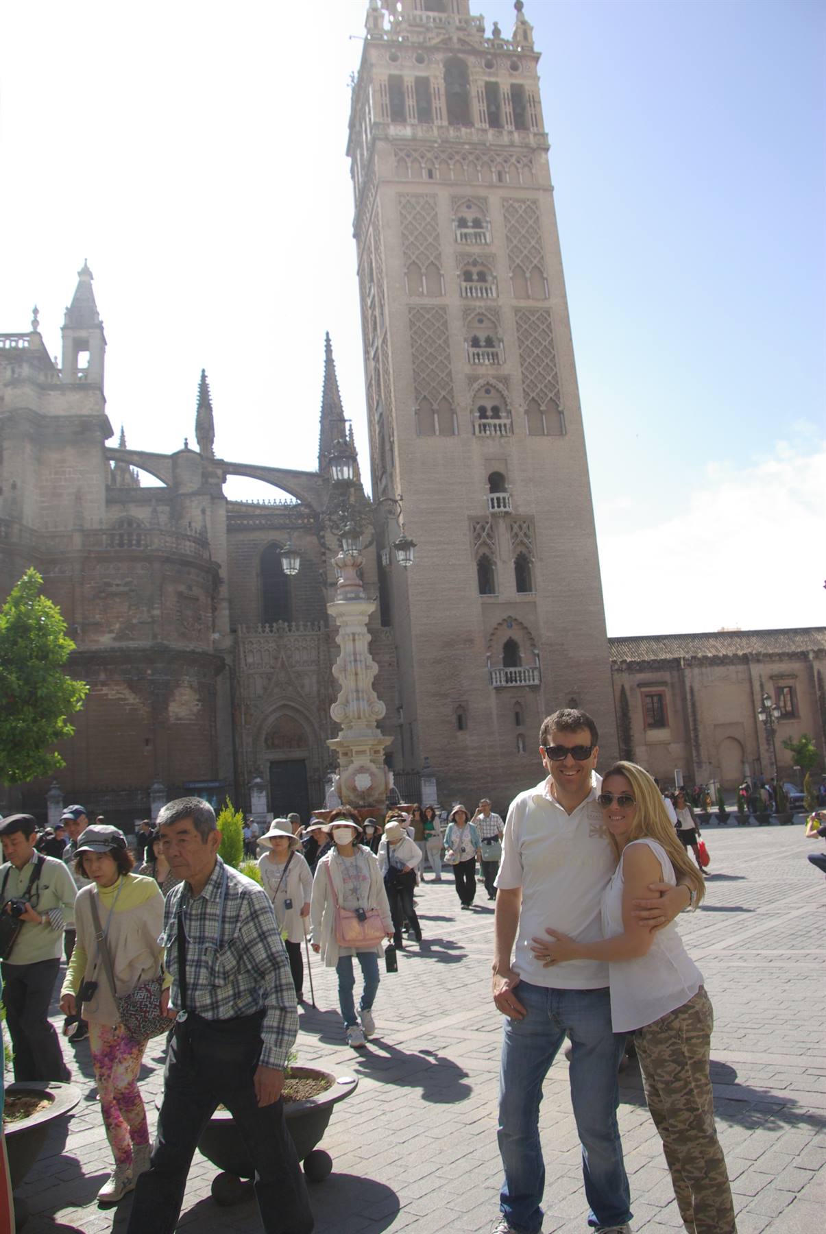 Coppia in posa davanti alla Giralda di Siviglia, turisti nella piazza assolata