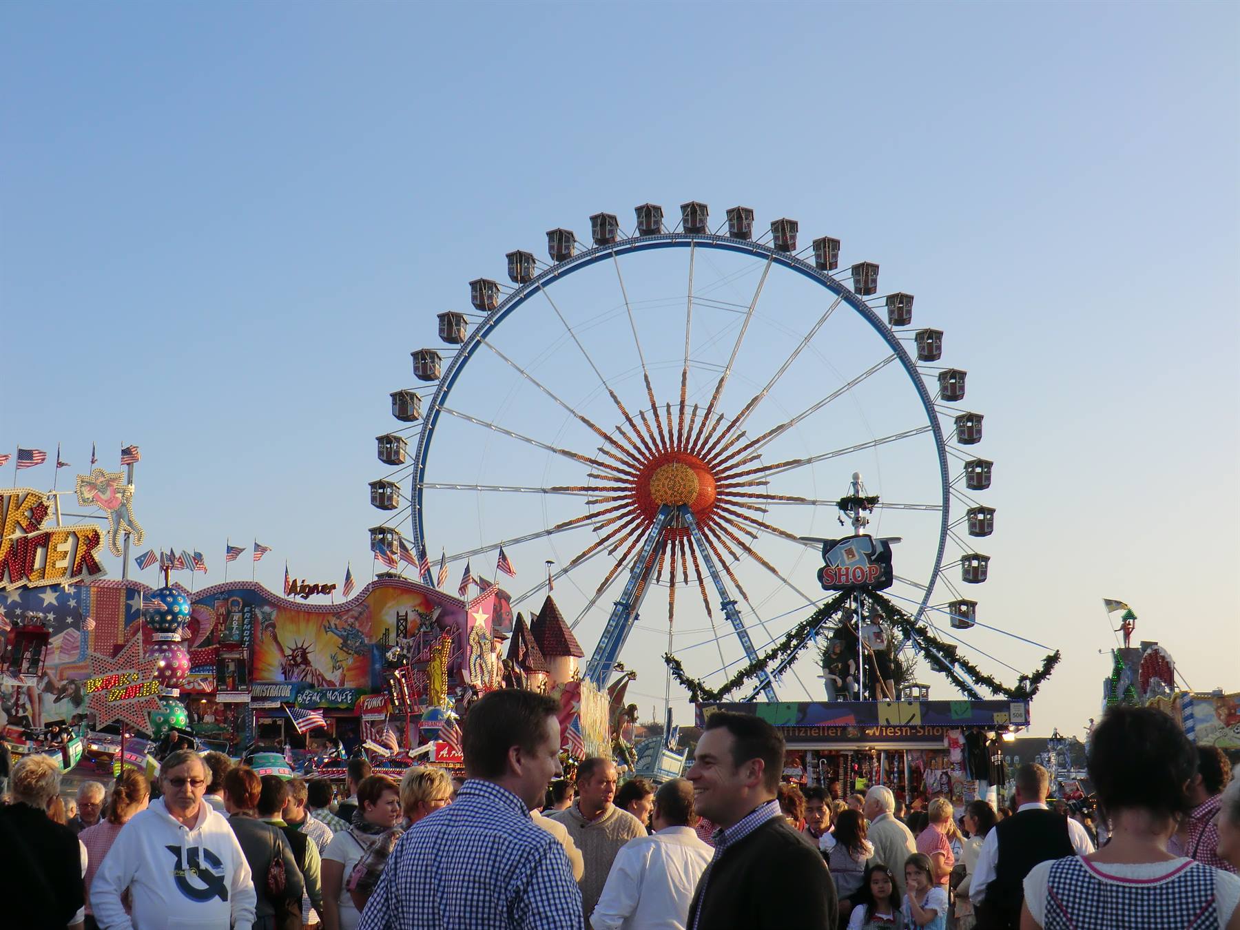 Folla alla fiera, grande ruota panoramica blu con cabine davanti a chioschi colorati