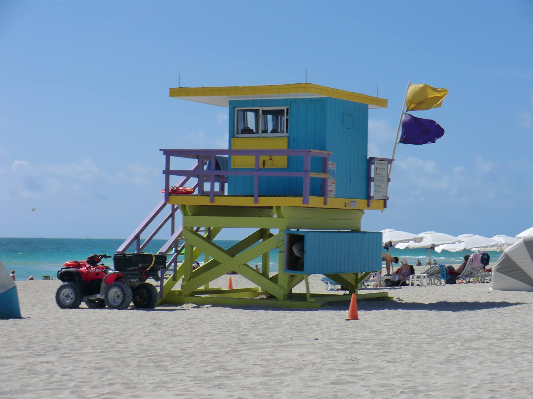 Torre bagnino azzurra su spiaggia sabbiosa, quad rosso accanto, ombrelloni e turisti