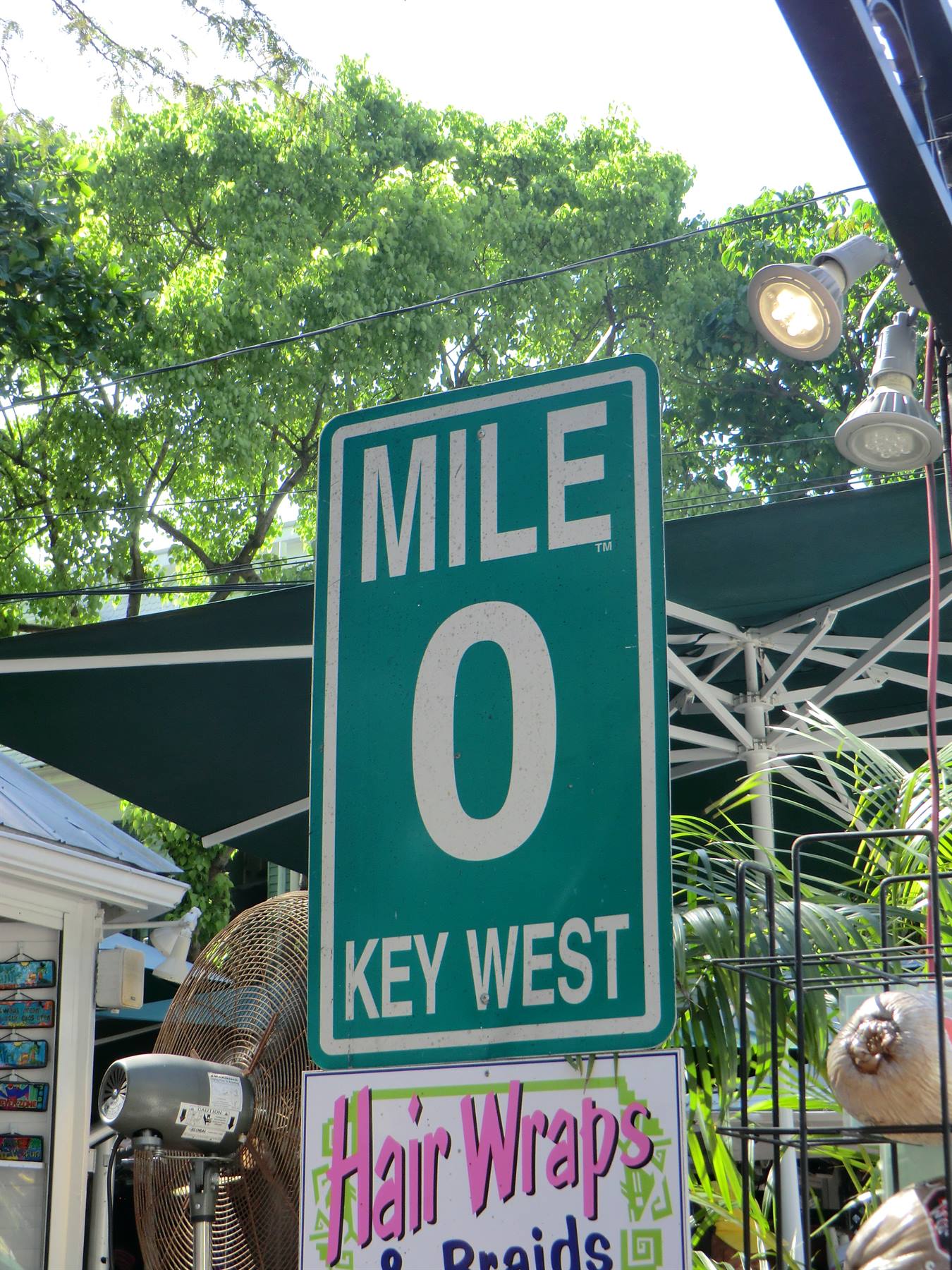 Cartello verde Mile 0 a Key West tra ombrelloni, ventilatori e alberi
