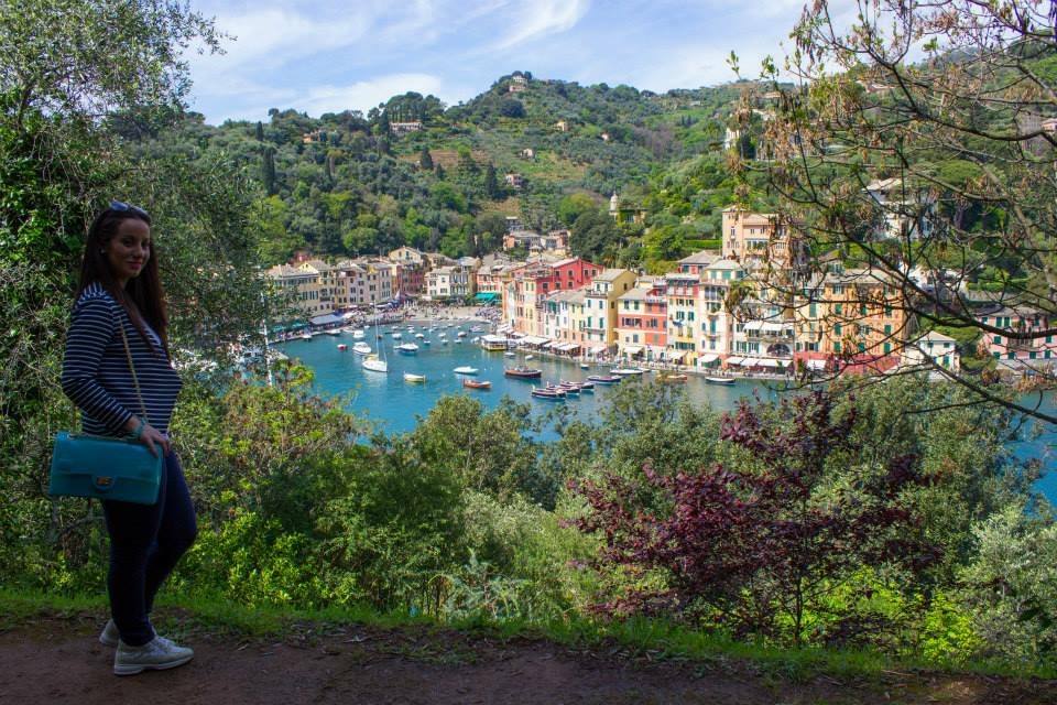 Donna sorridente con borsa turchese su sentiero sopraelevato, dietro il porto di Portofino