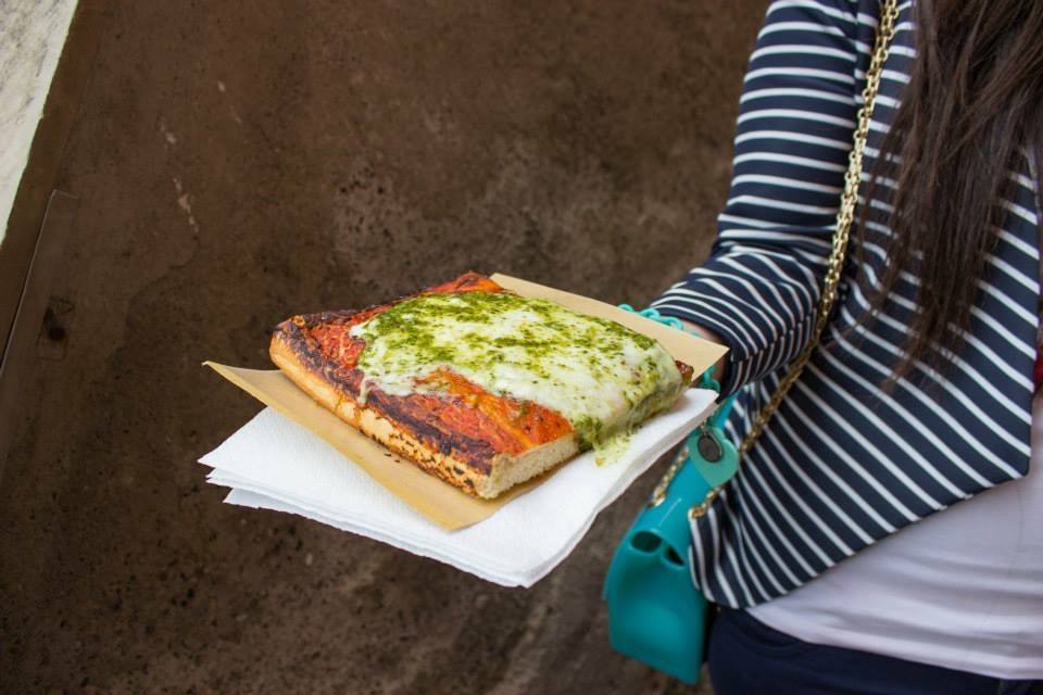 Donna in maglia a righe con borsa turchese tiene una focaccia al pesto su tovagliolo