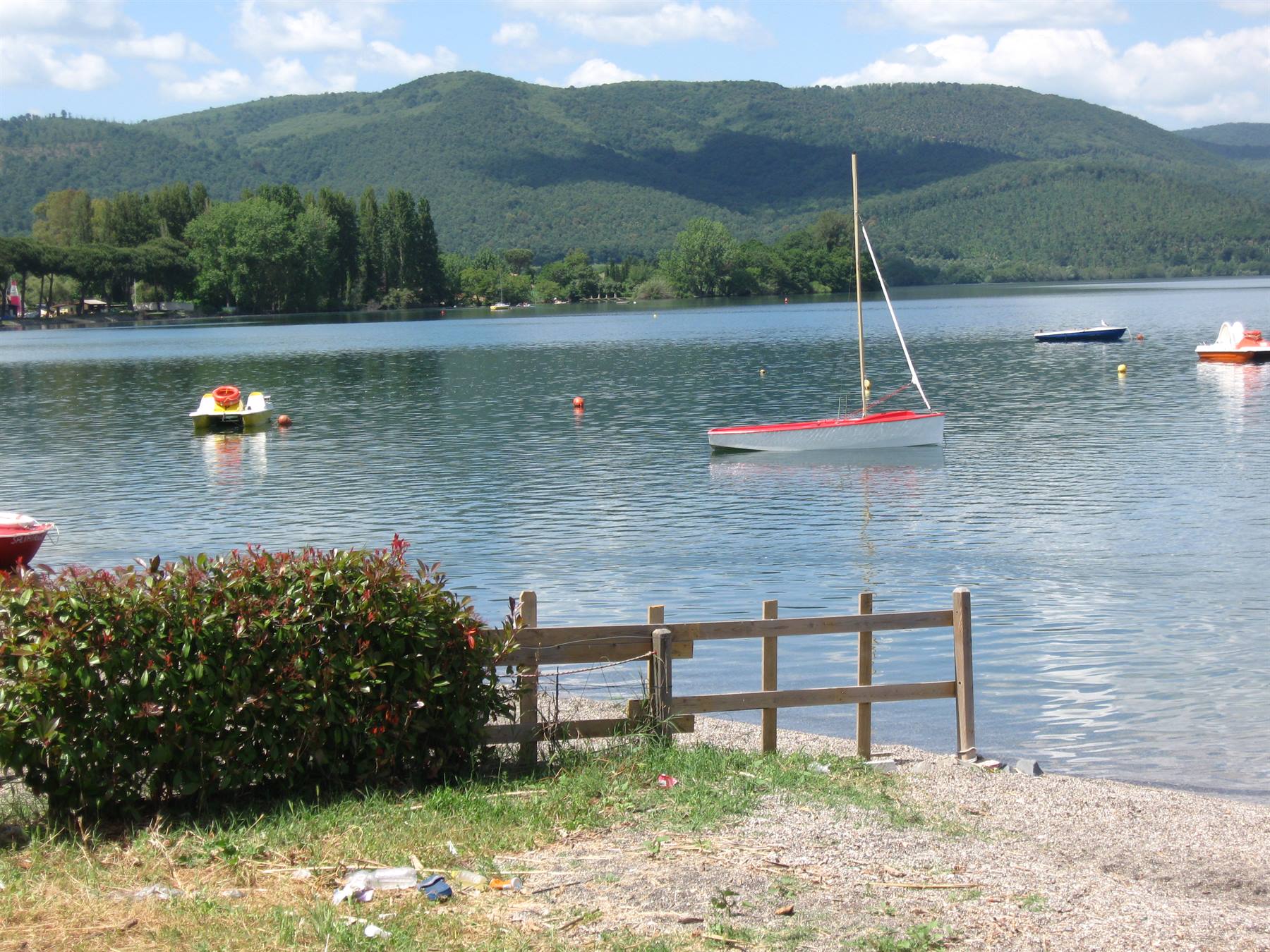 Barca a vela rossa e bianca ancorata sul lago, recinzione di legno sulla riva
