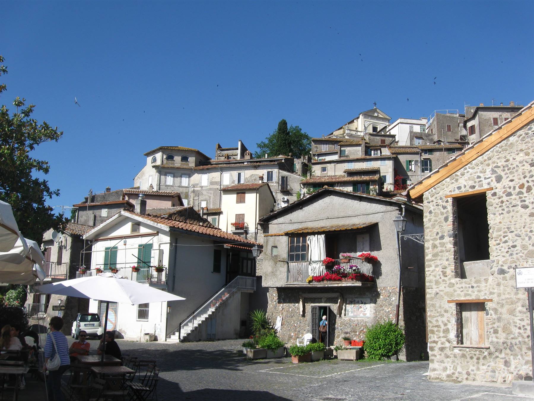 Piazzetta con ombrelloni sotto case in pietra e mattoni del borgo arroccato