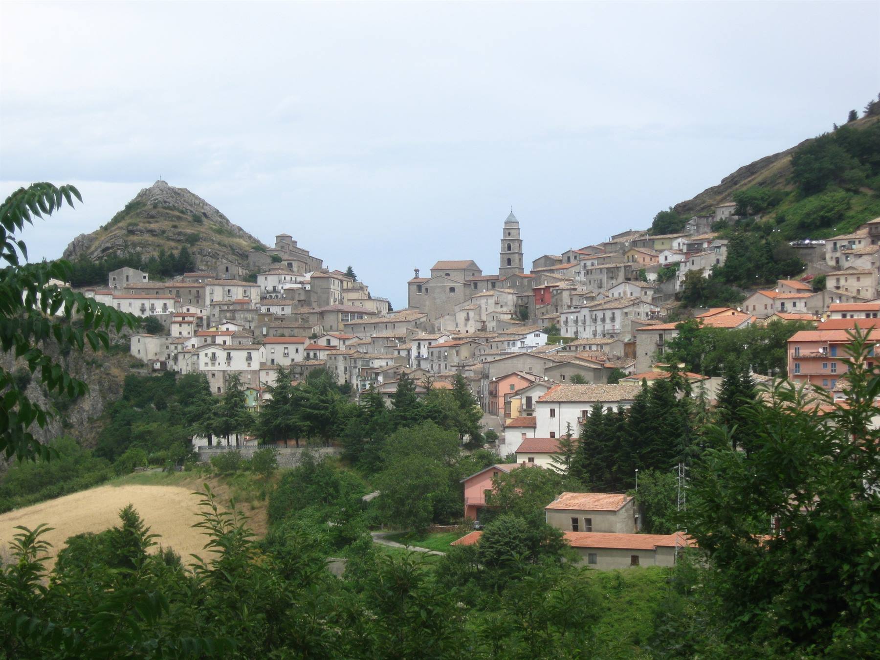 borgo di case in pietra con campanile tra le montagne, cielo grigio