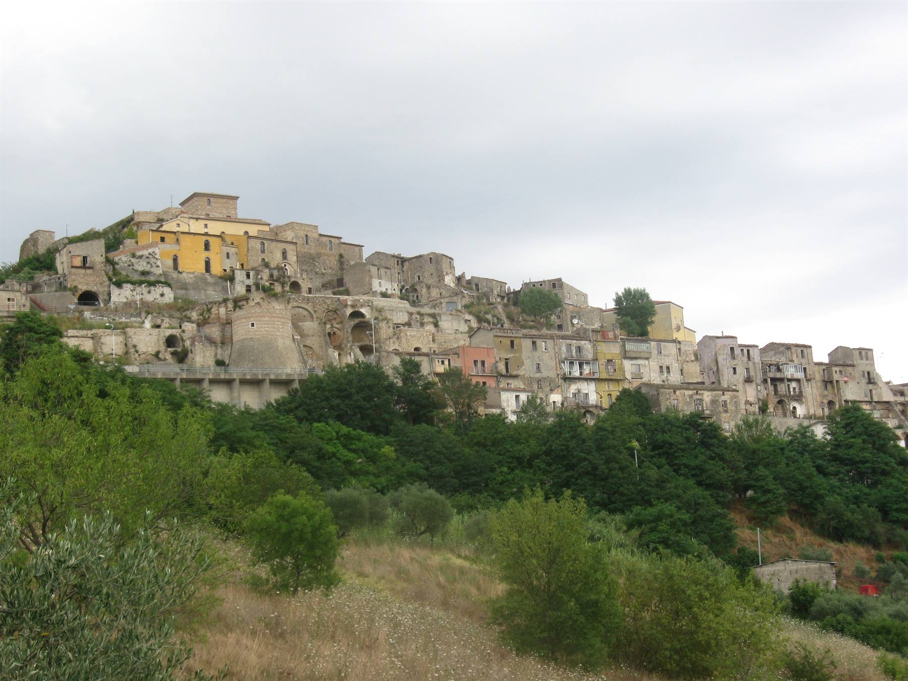 Village abbandonato in pietra su una collina, sopra alberi verdi e cespugli