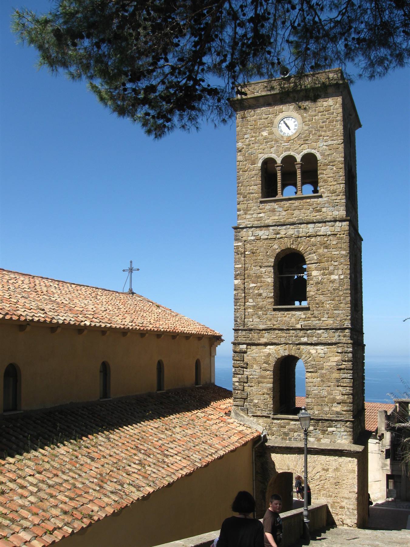 Campanile in pietra con orologio e tetti di tegole sopra il mare