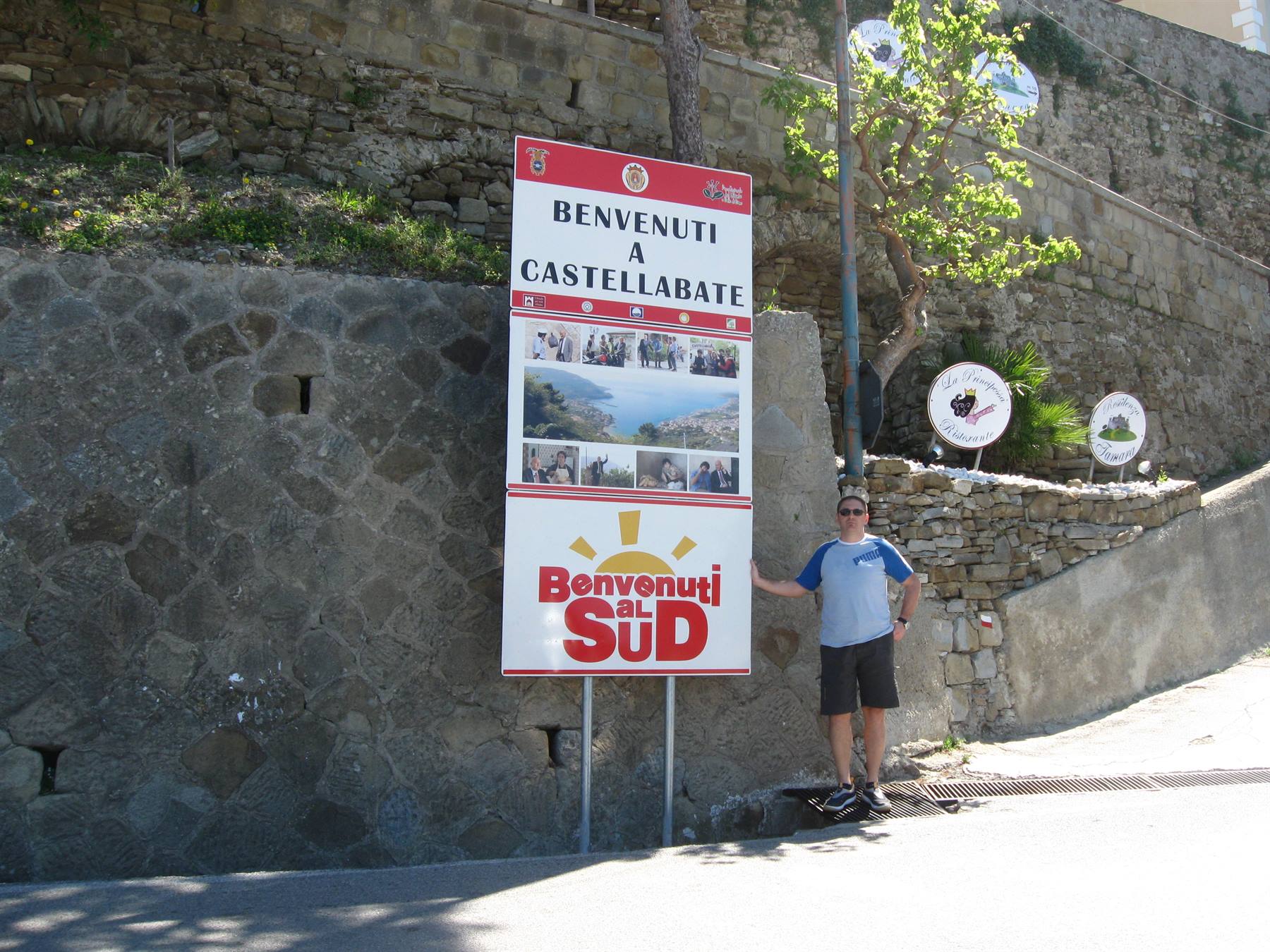 Turista accanto al cartello Benvenuti a Castellabate su muro di pietra