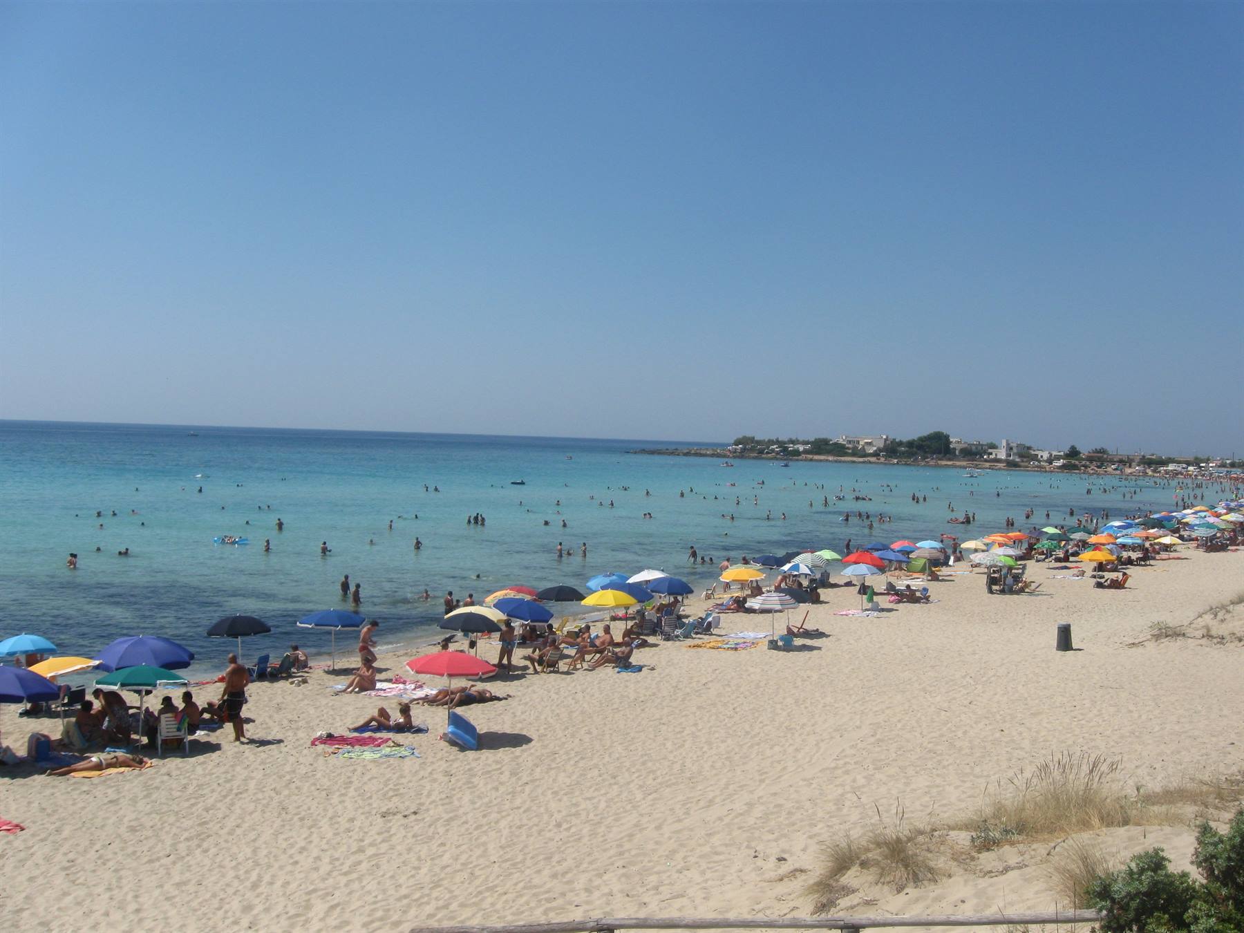 Spiaggia affollata di sabbia chiara, ombrelloni colorati e bagnanti nel mare turchese