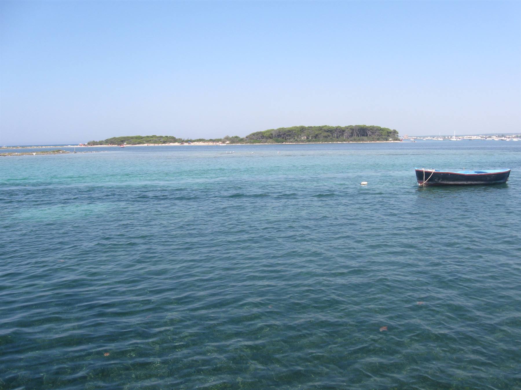 Barca di legno ancorata su mare turchese, isola verde sullo sfondo