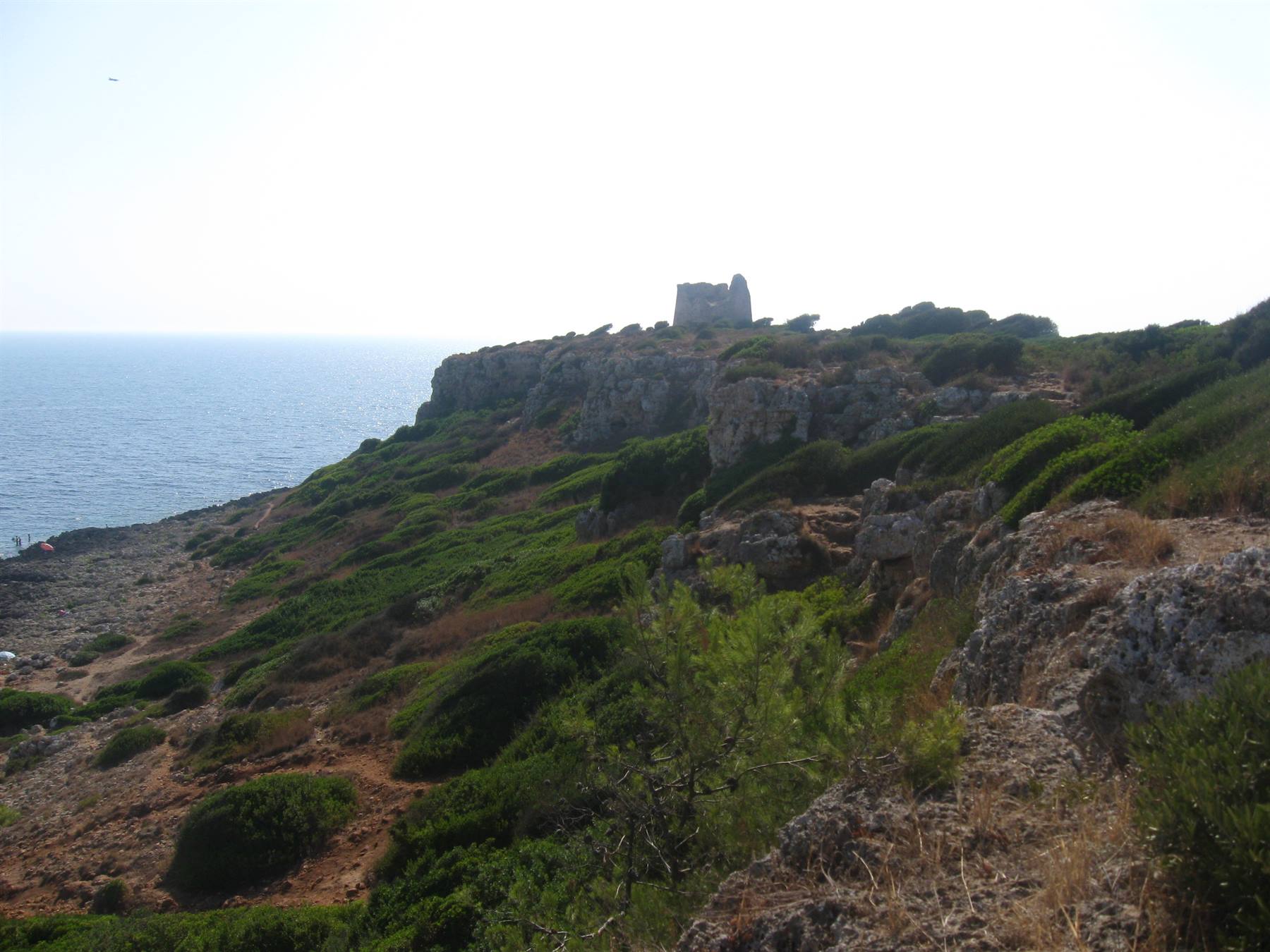 Antica torre costiera in pietra su scogliera con macchia mediterranea sopra il mare