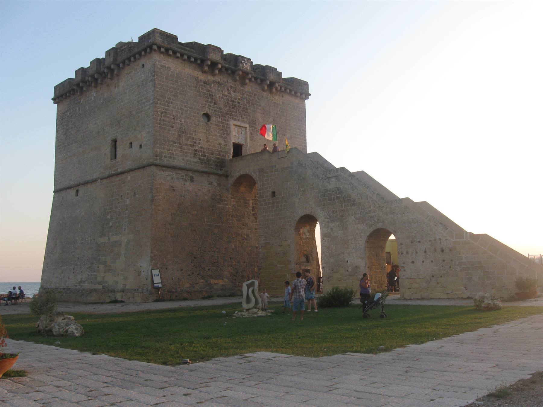 Turisti sotto l'antica torre costiera in pietra con bandiera italiana