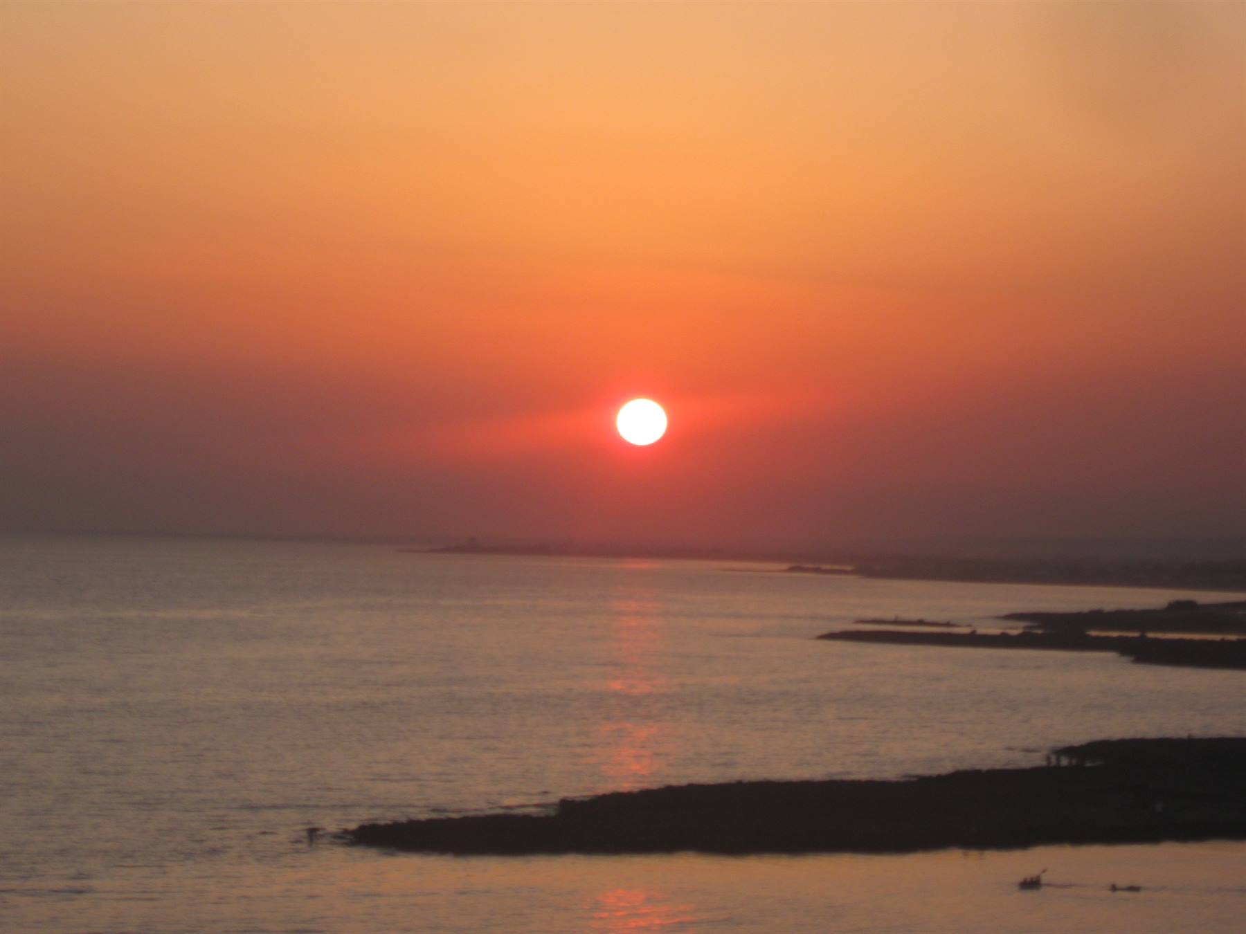 Sole basso riflesso sul mare calmo davanti a scogliere scure